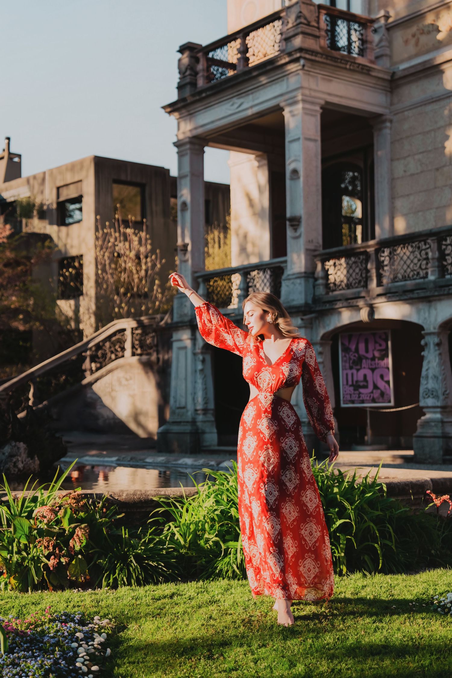 Woman in red floral maxi dress poses in front of a grand historic stone building.