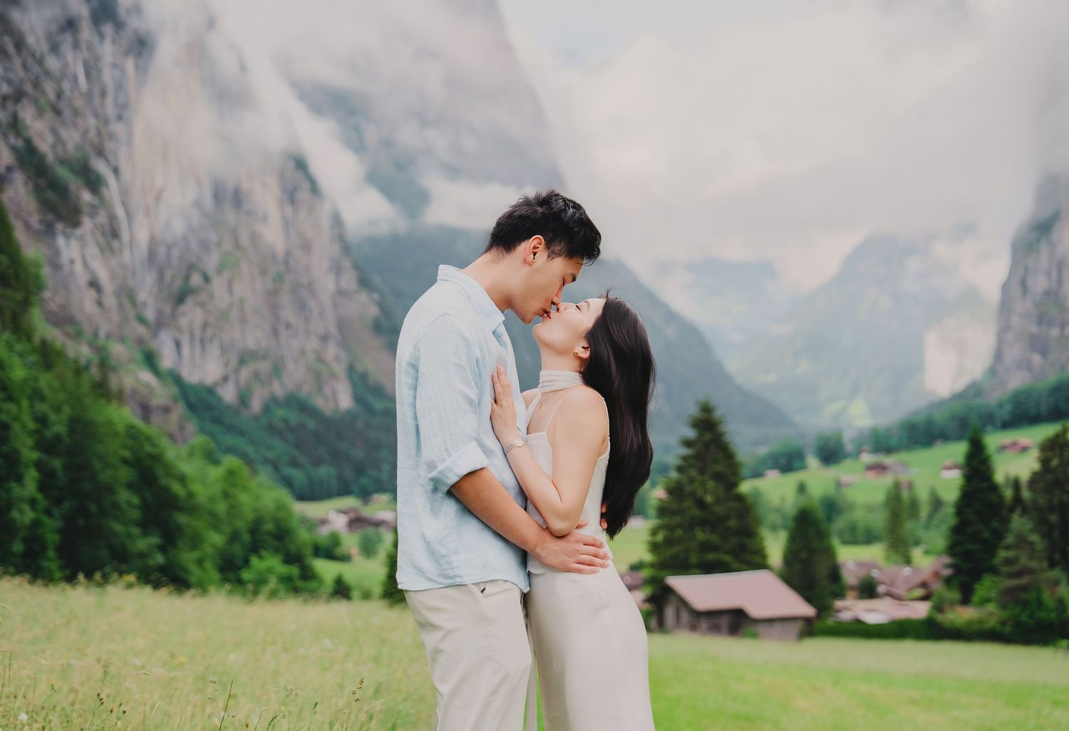 Romantic couple sharing a kiss in a green alpine valley with dramatic mountain cliffs in Switzerland.