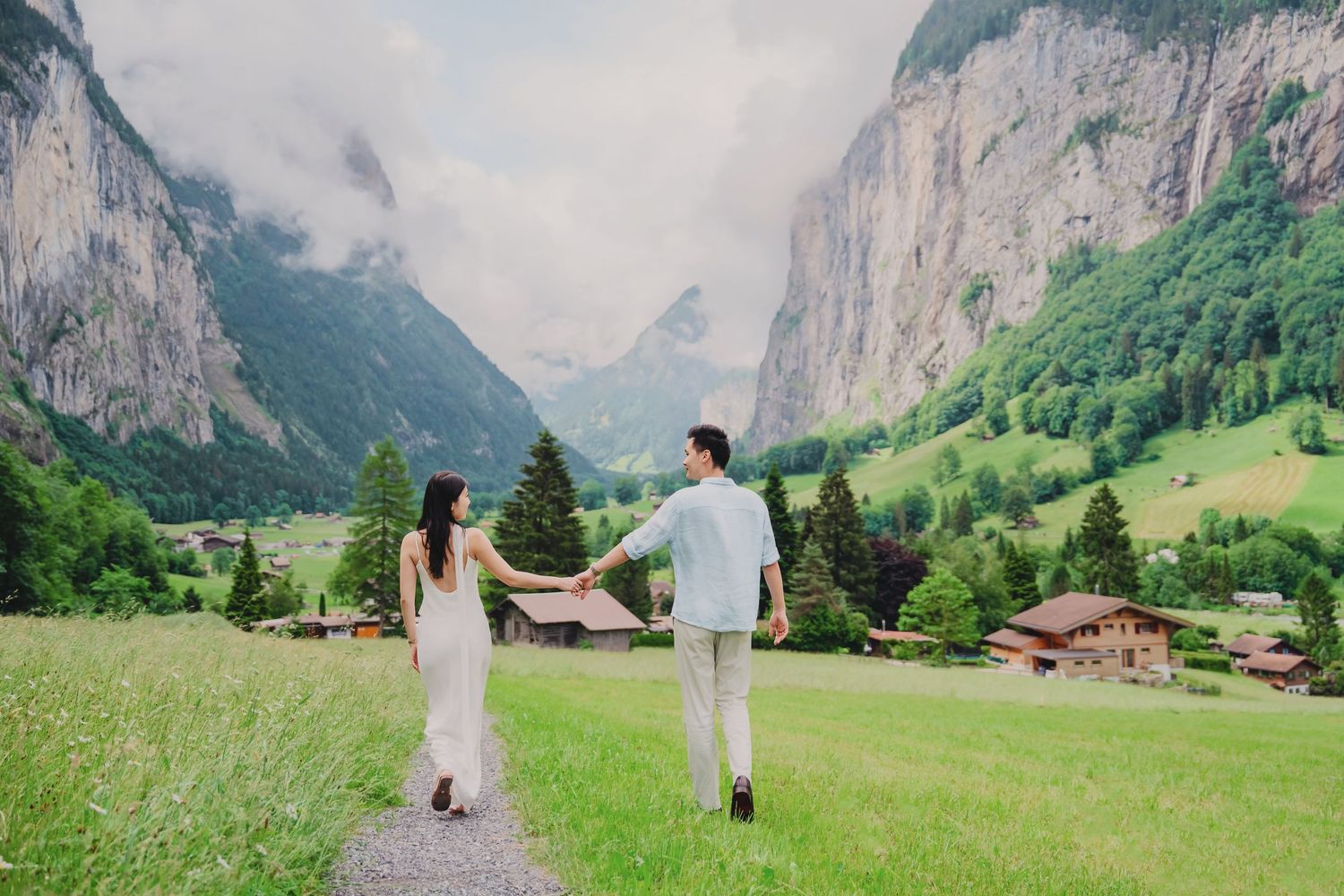 Couple holding hands walking on a path through a lush Swiss alpine valley with dramatic cliffs.