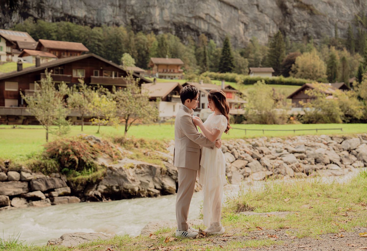 Couple sharing a tender embrace by a rocky riverbank in a Swiss alpine village.