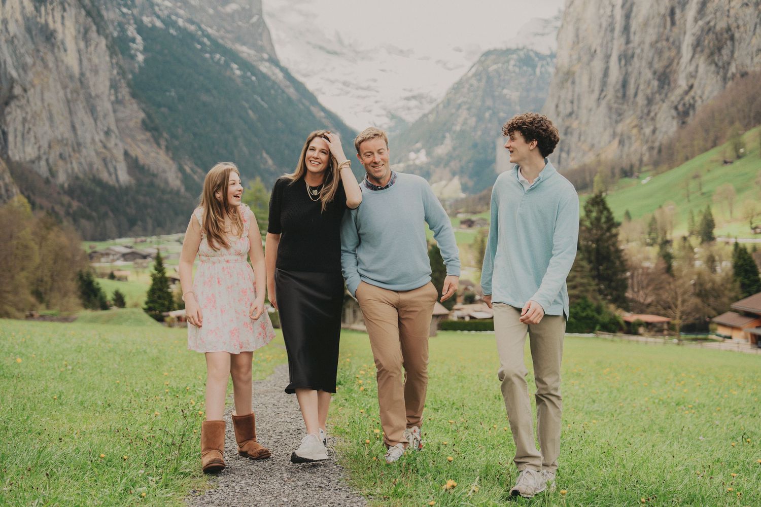 Cheerful family of four laughing while walking through a beautiful green Swiss alpine meadow together.