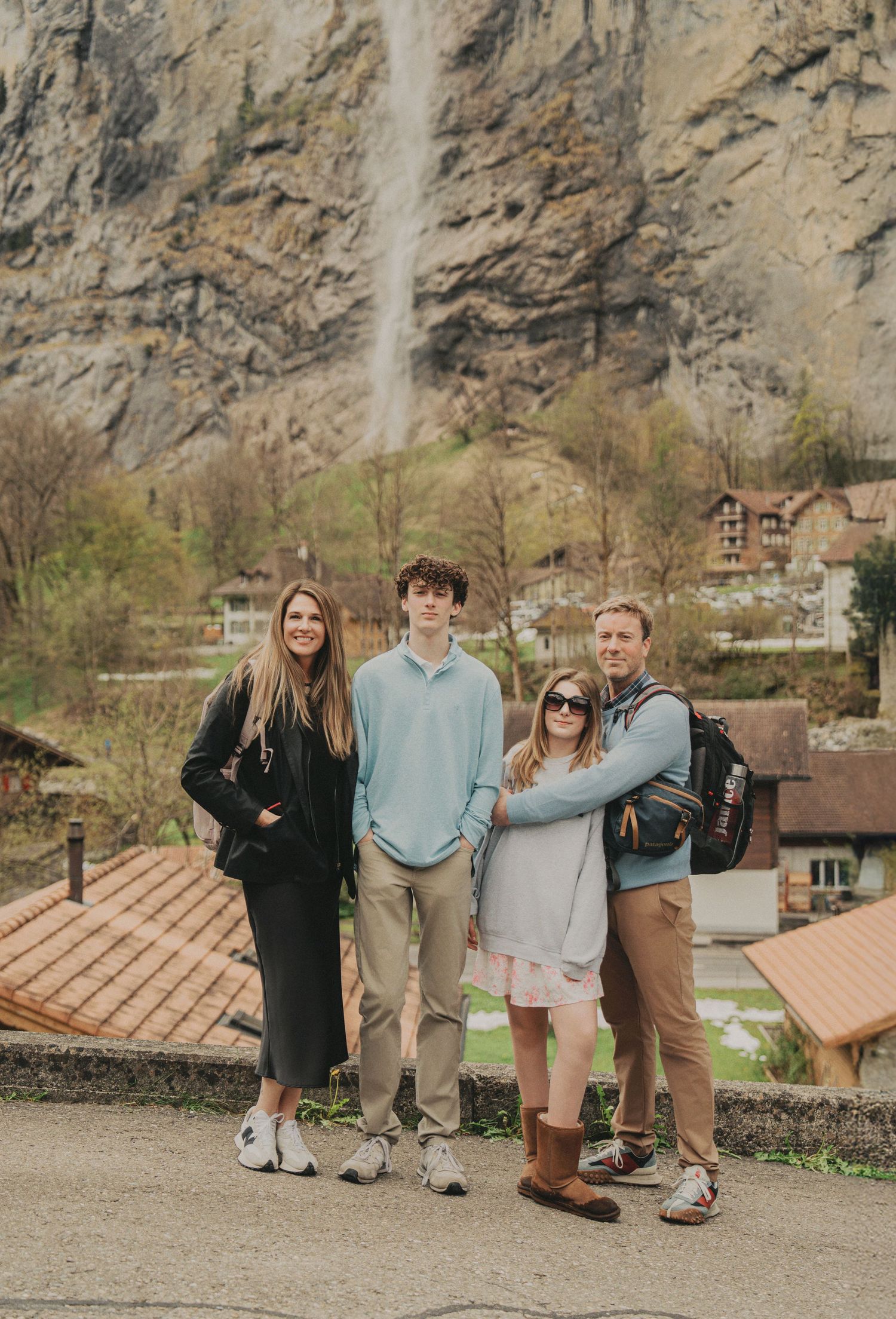Family smiling together with a scenic Swiss waterfall and village in the background.
