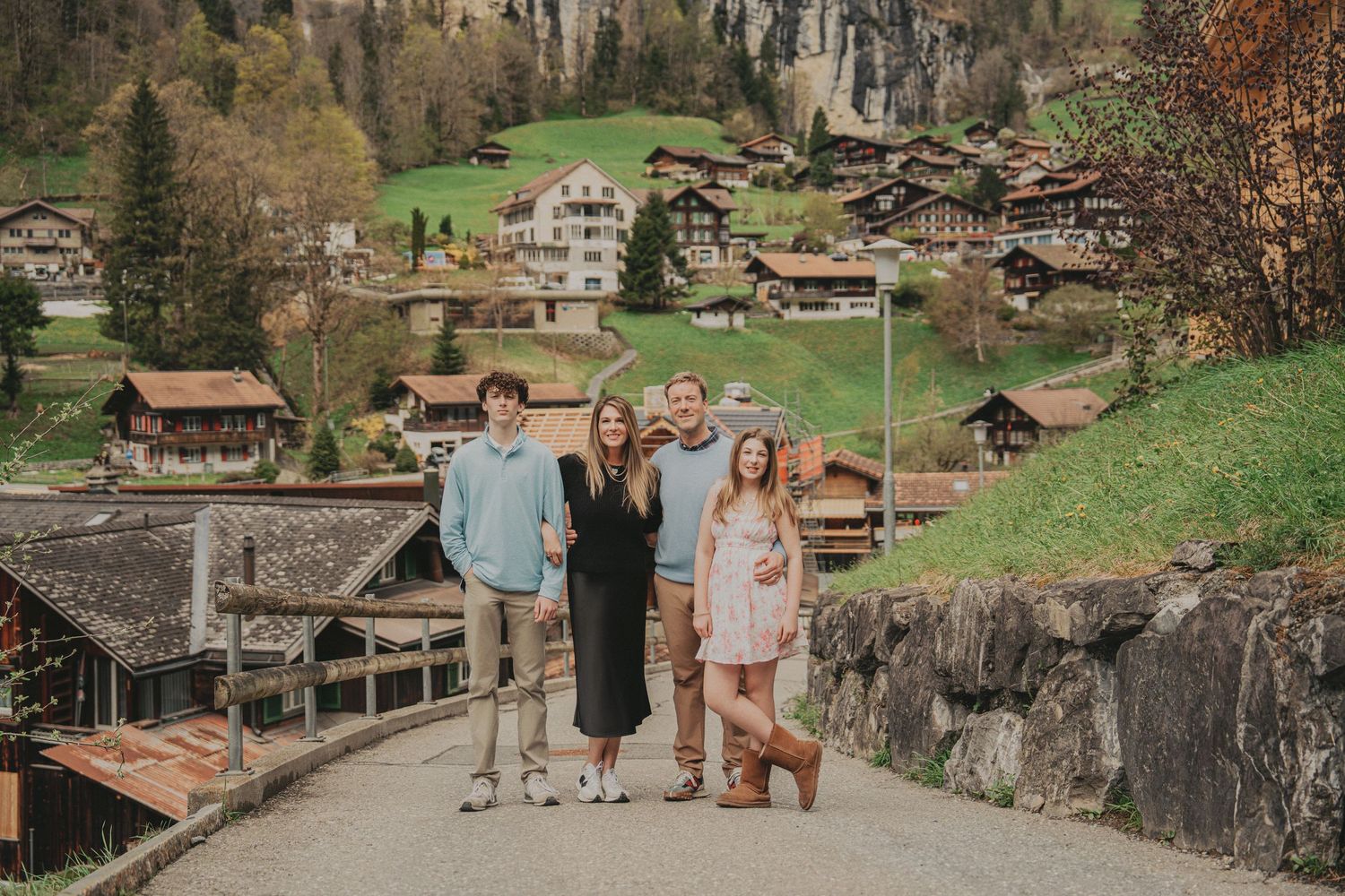 Family of four posing on a road with charming Swiss chalet village and autumn mountains behind them.