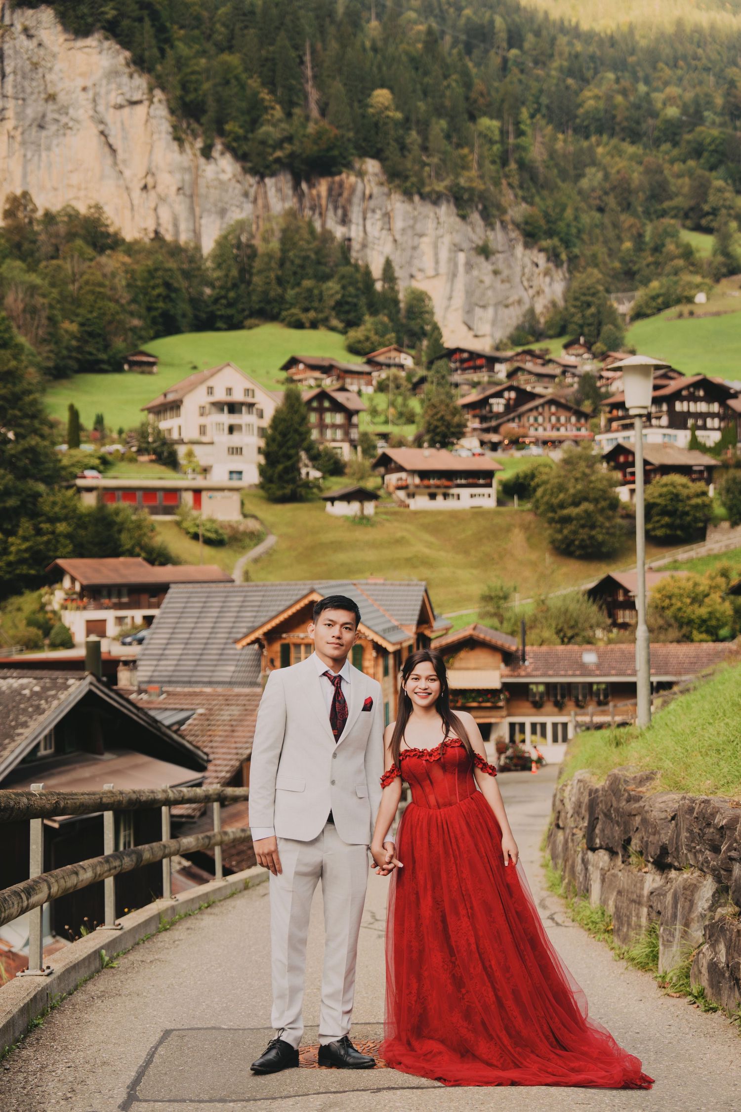 Couple posing on a road in Lauterbrunnen with stunning Swiss alpine village and cliffs in background.
