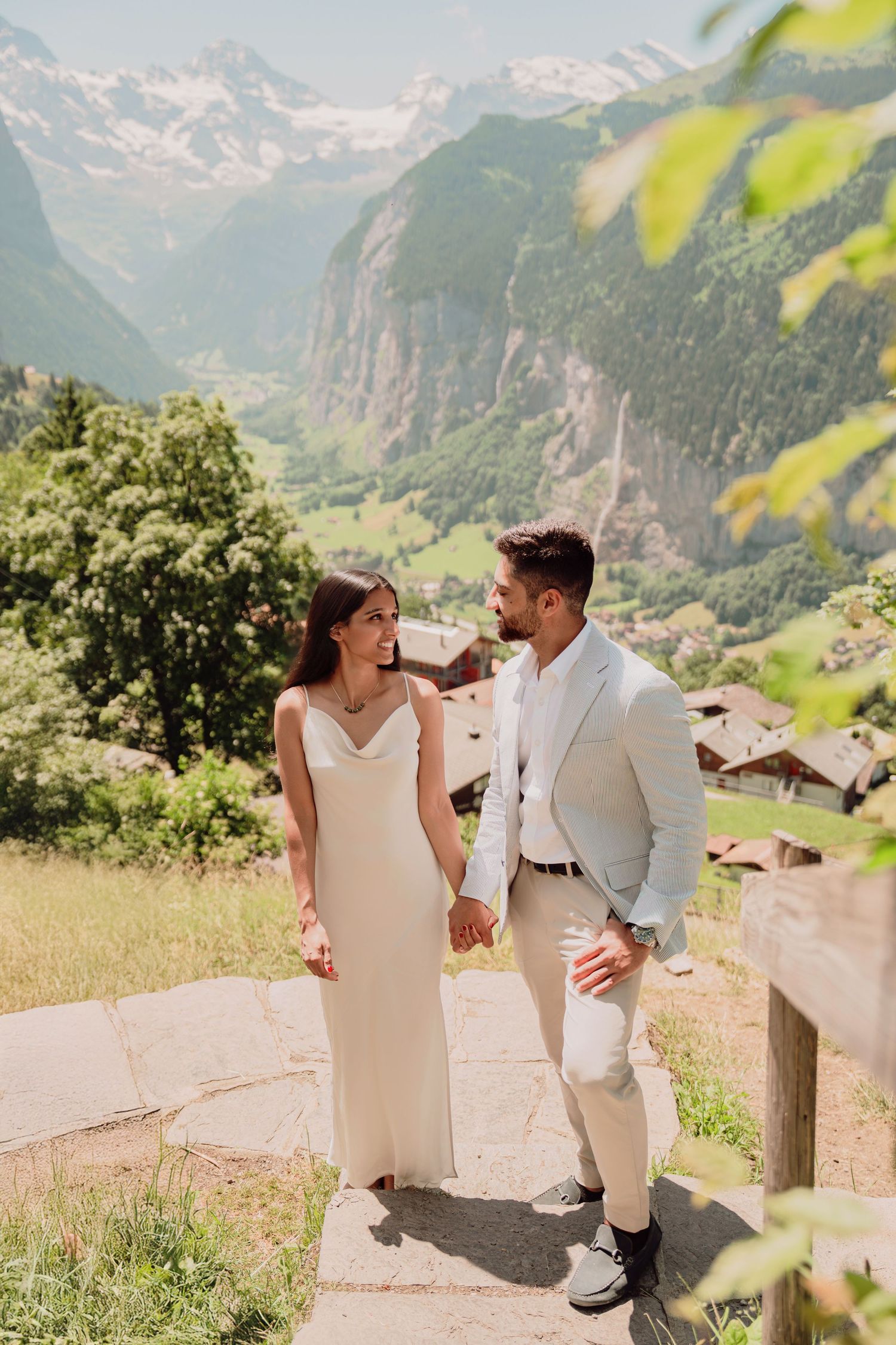 Bride and groom holding hands walking on stone path with Lauterbrunnen valley view behind them.