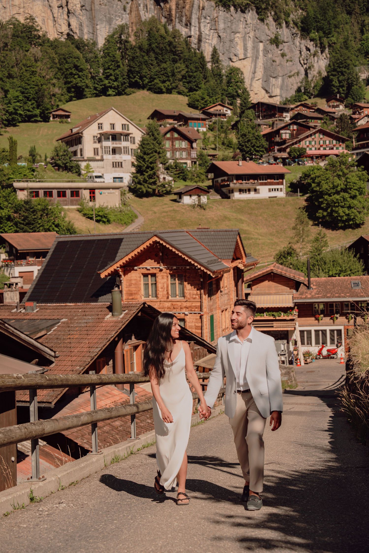 Couple walking hand in hand through charming Swiss village of Lauterbrunnen with alpine chalets.