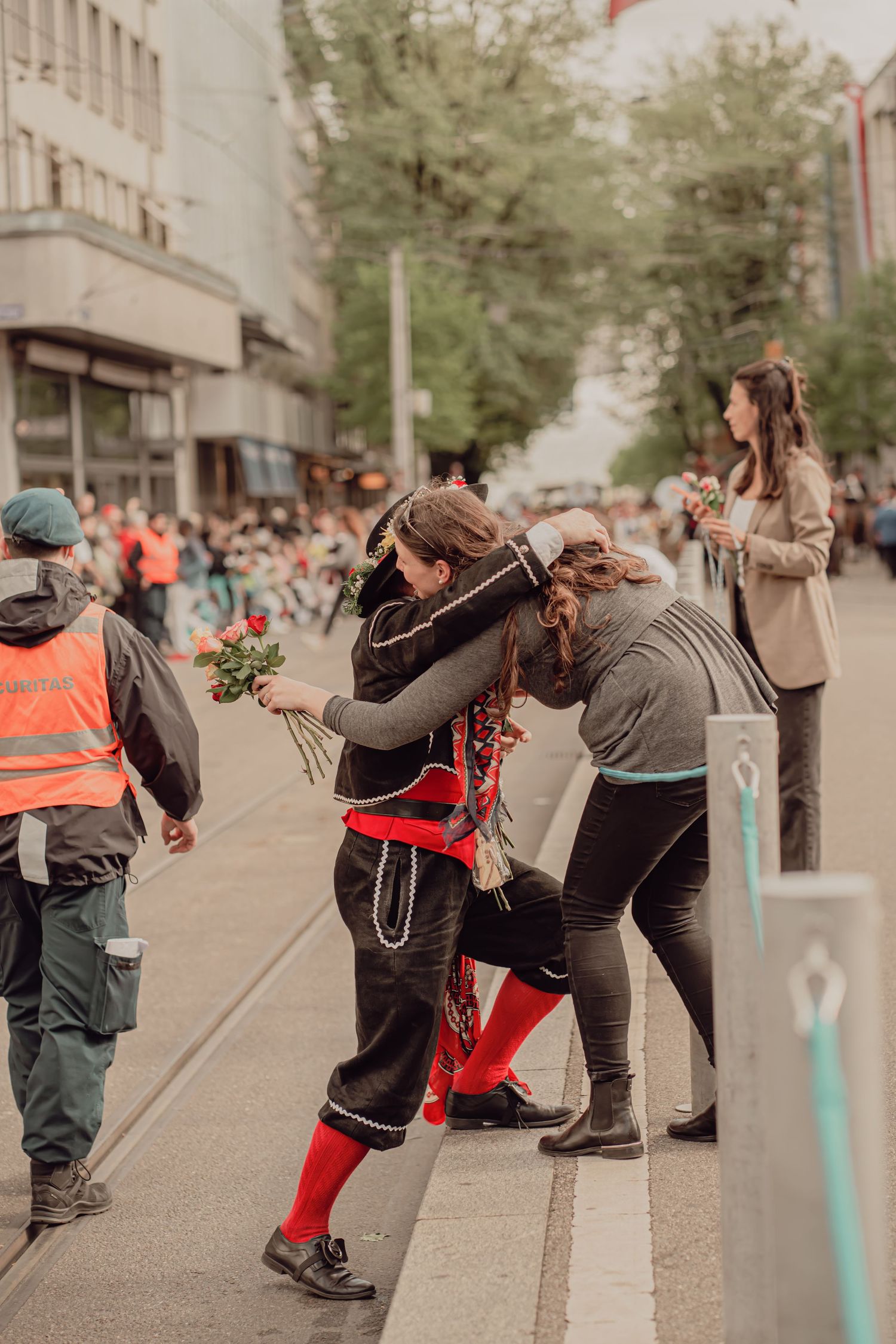 Person in traditional Swiss folk costume embraces a spectator while holding red roses at a parade.