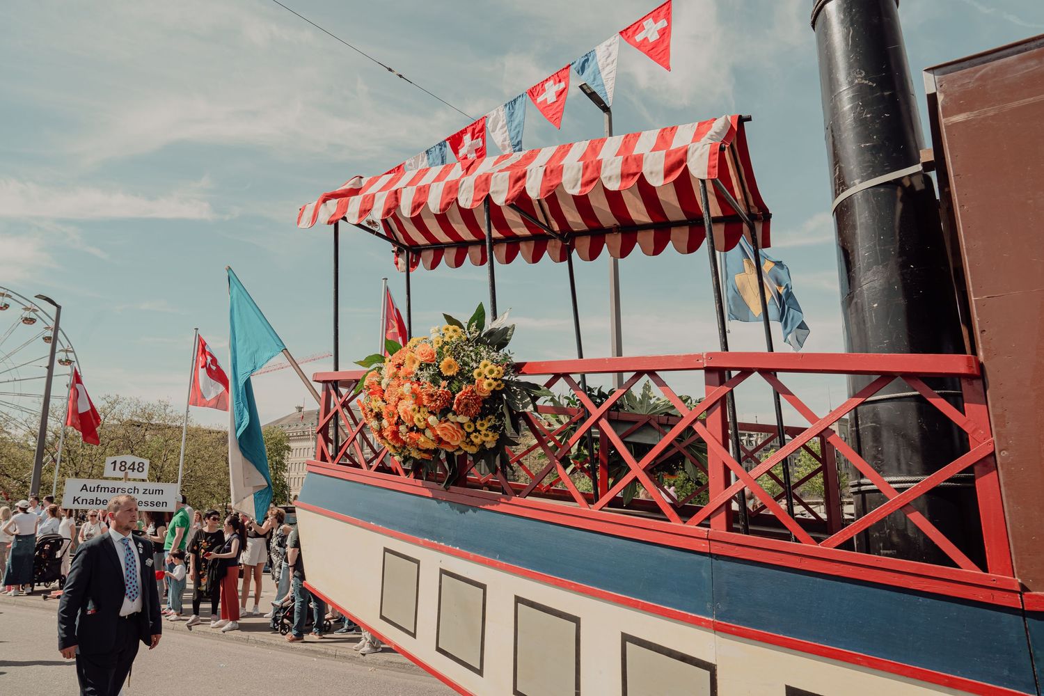 Decorated parade float designed as a vintage steamboat adorned with orange flowers and Swiss flags outdoors.
