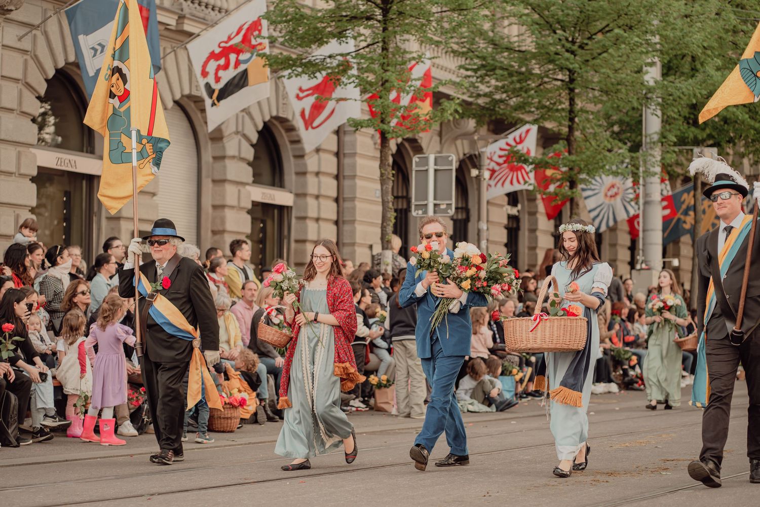 Colorful procession of people in historical costumes carrying flowers through a festive street parade.