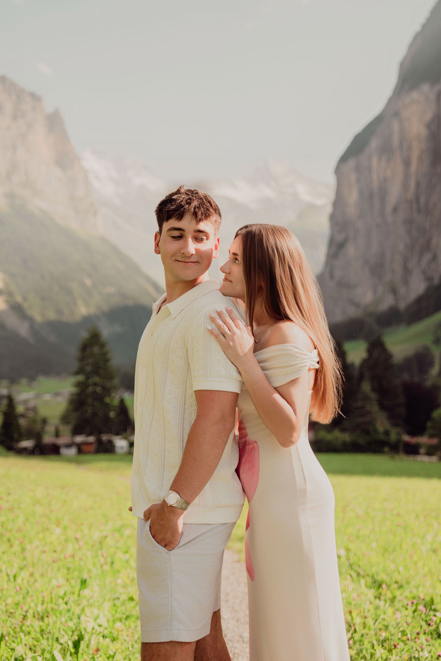 Couple sharing a tender moment on a path through green alpine meadow with mountain views.