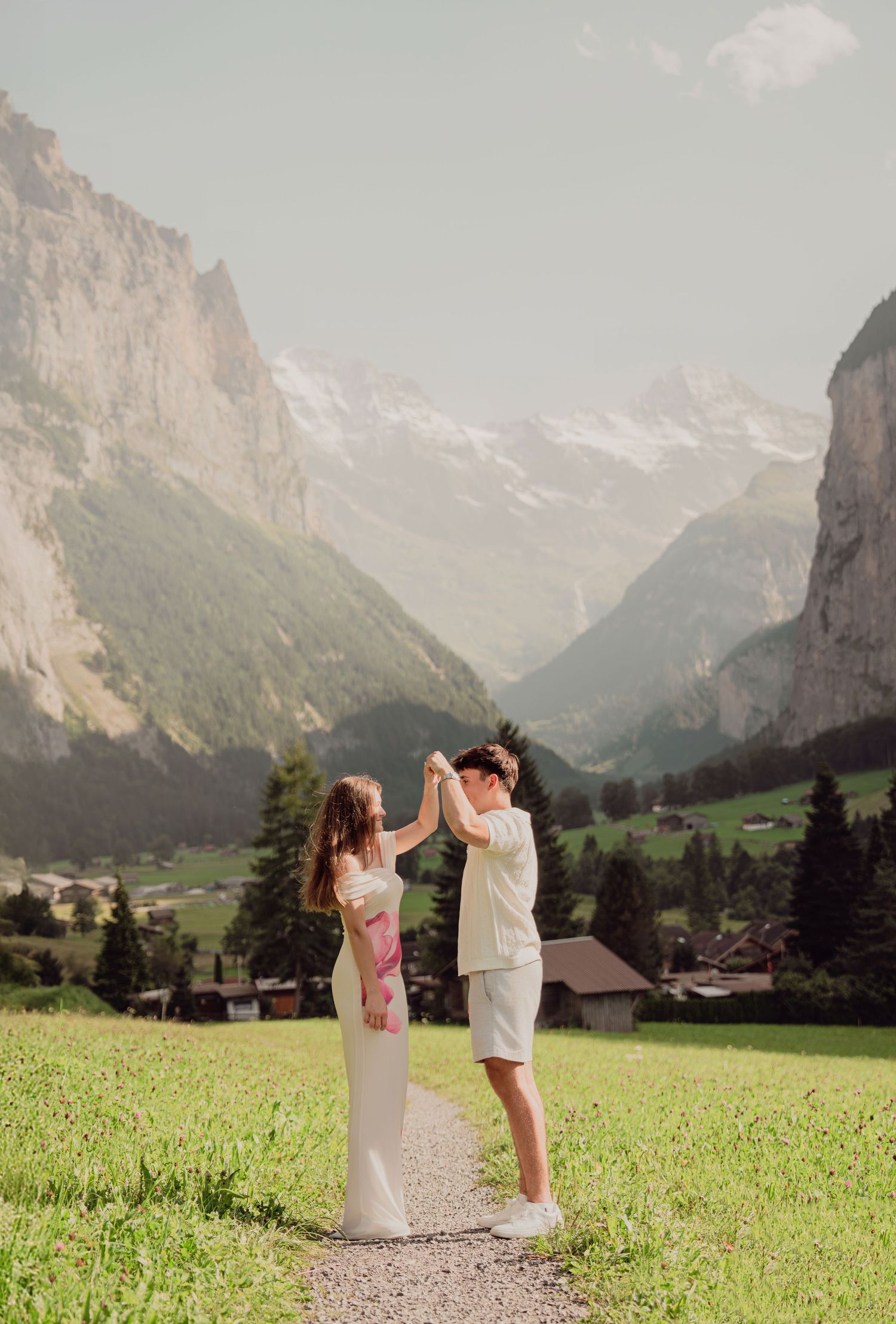 Young couple holding hands and dancing on a scenic path in the Swiss Alps with valley views.
