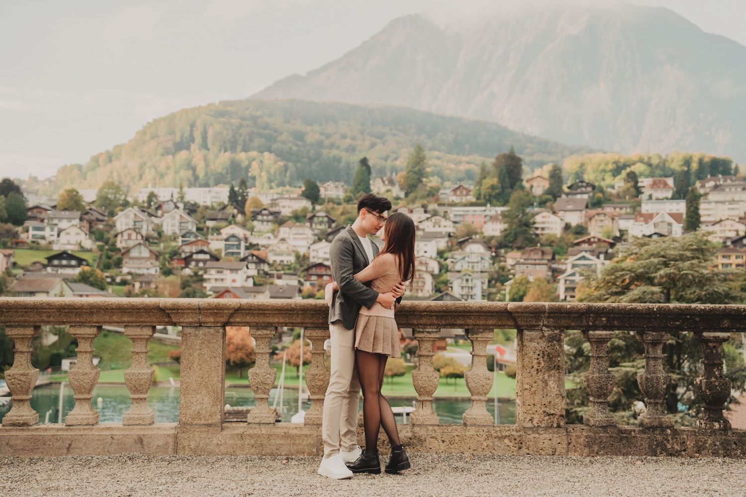 Romantic couple embracing on classic stone terrace with charming Alpine town and mountain scenery.