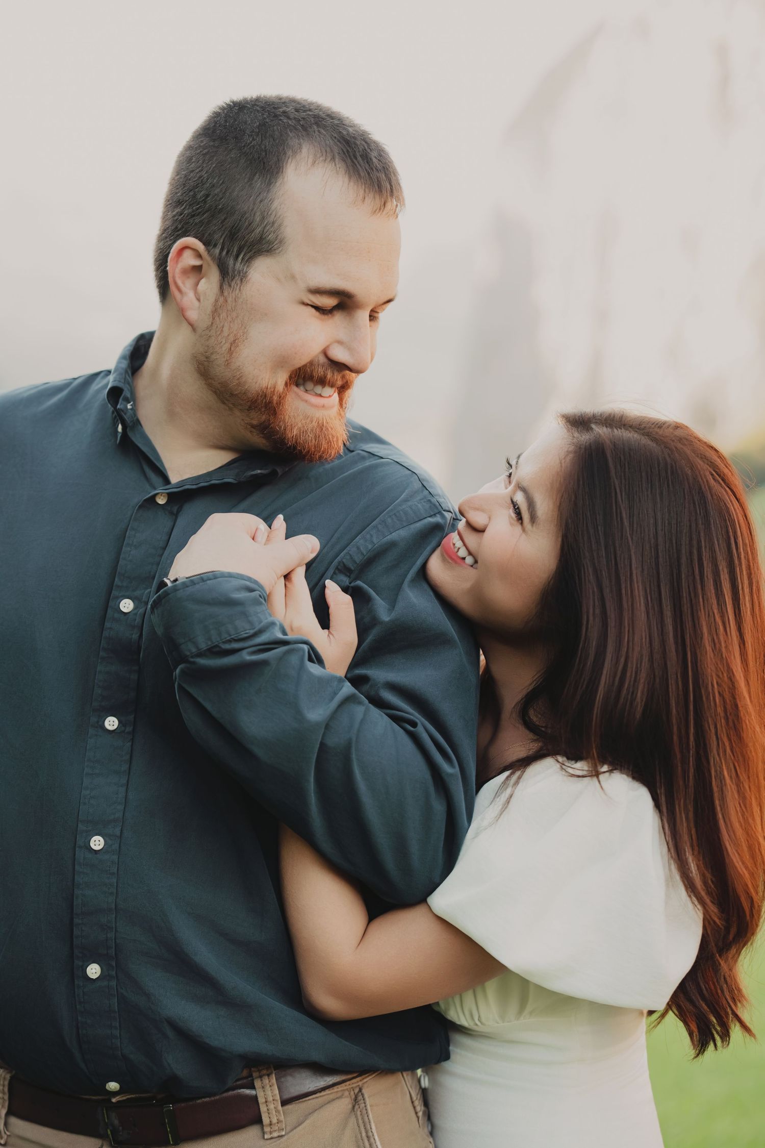 Joyful couple laughing and embracing closely in a soft outdoor setting.
