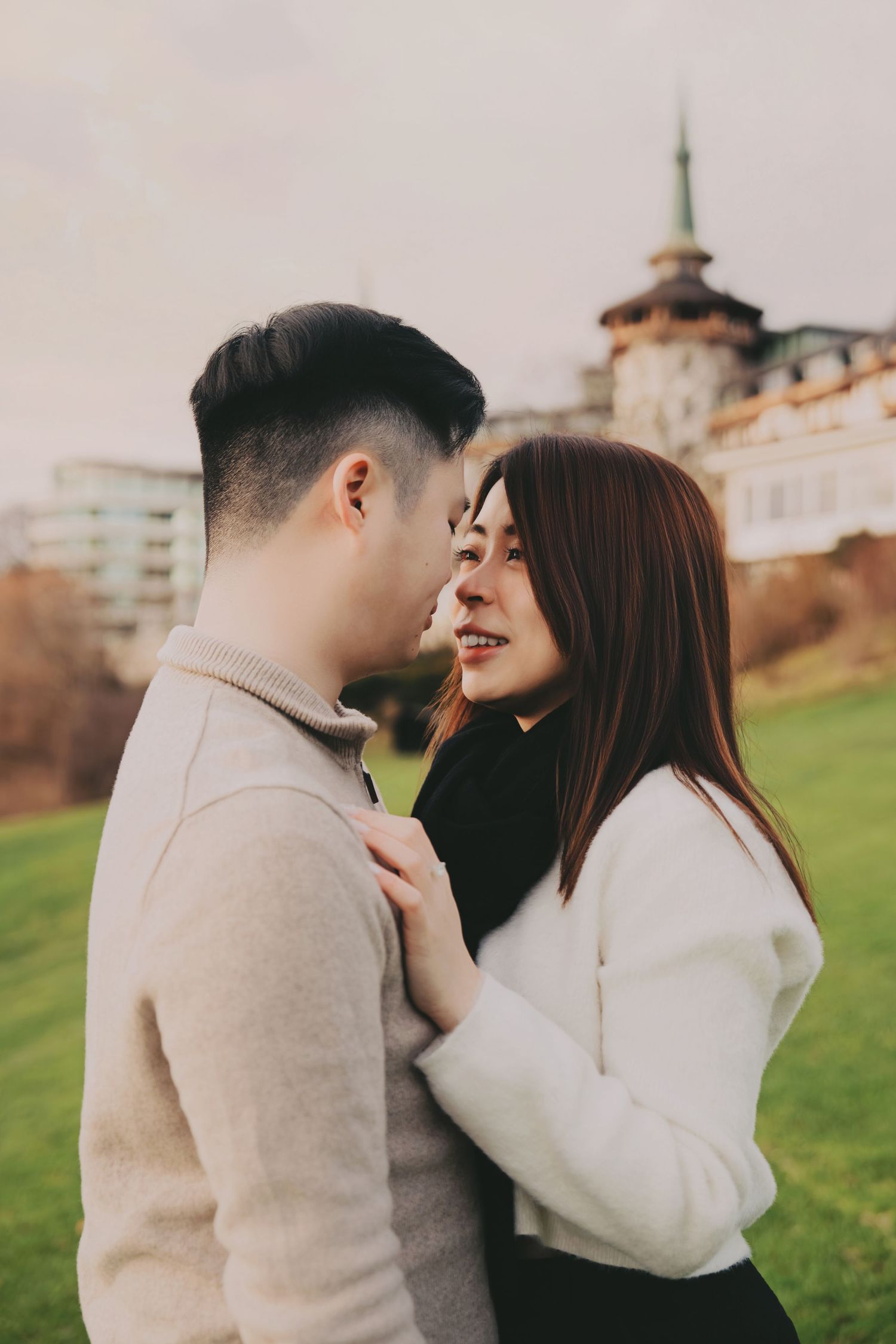 Happy couple embracing and smiling at each other on green lawn near a grand historic building.