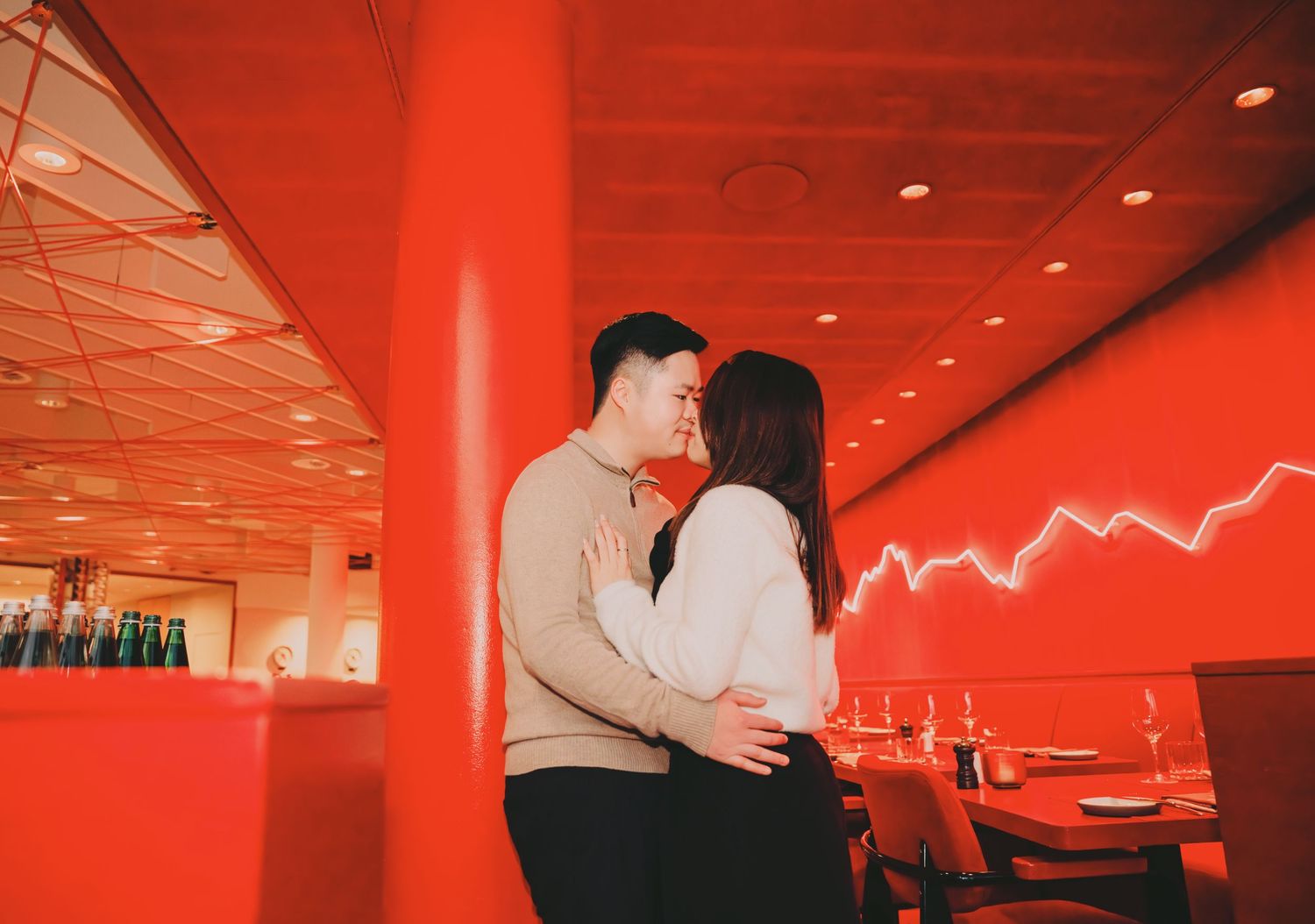 Romantic couple sharing a kiss in a vibrant red restaurant interior with neon light decor.