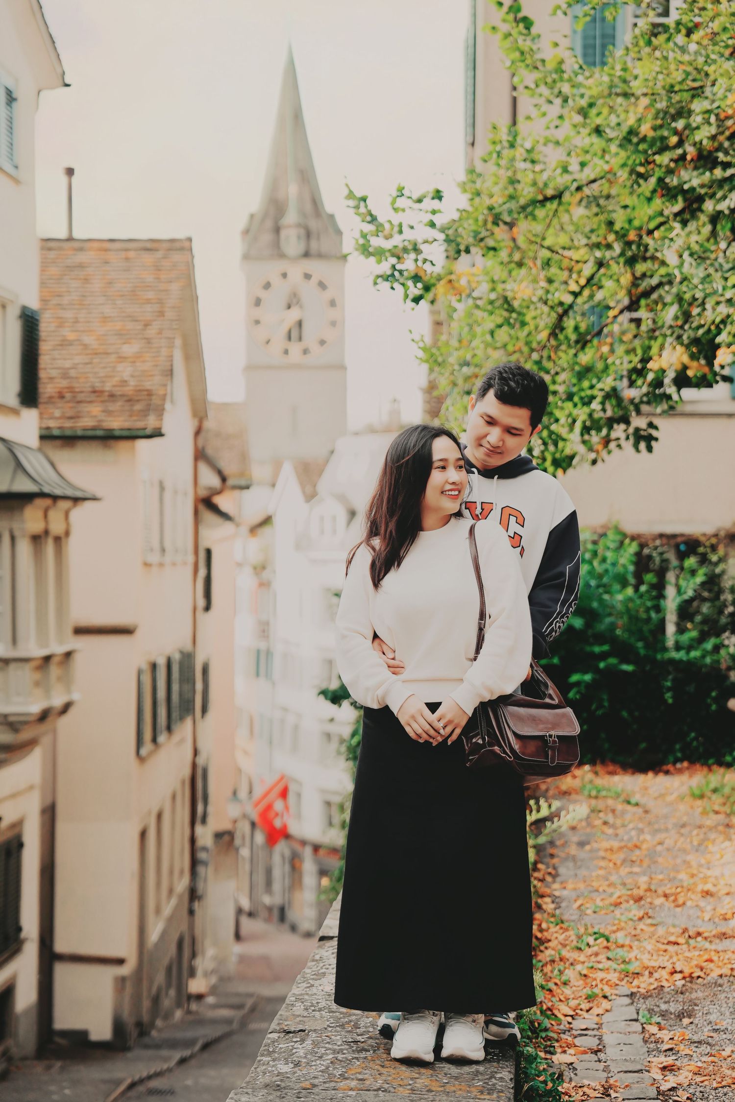 Couple sharing a tender moment on stone steps in Zurich's historic district with clock tower in the background.