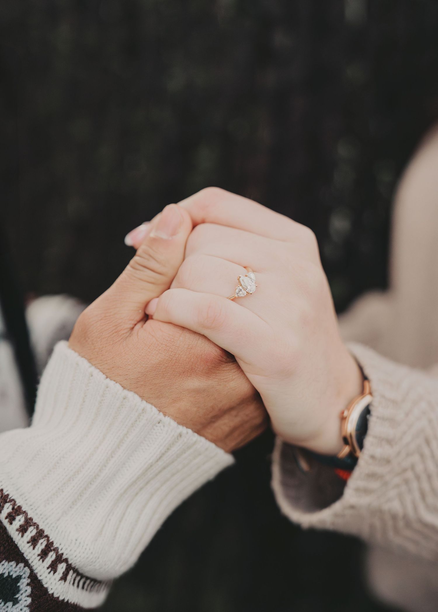 Close-up of couple holding hands showing engagement ring on cobblestone street.