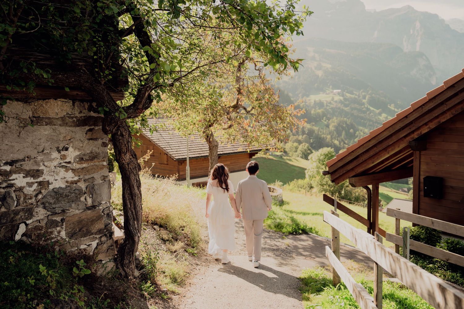 Couple walking hand in hand along scenic Swiss countryside path with lush green meadows and mountain views.