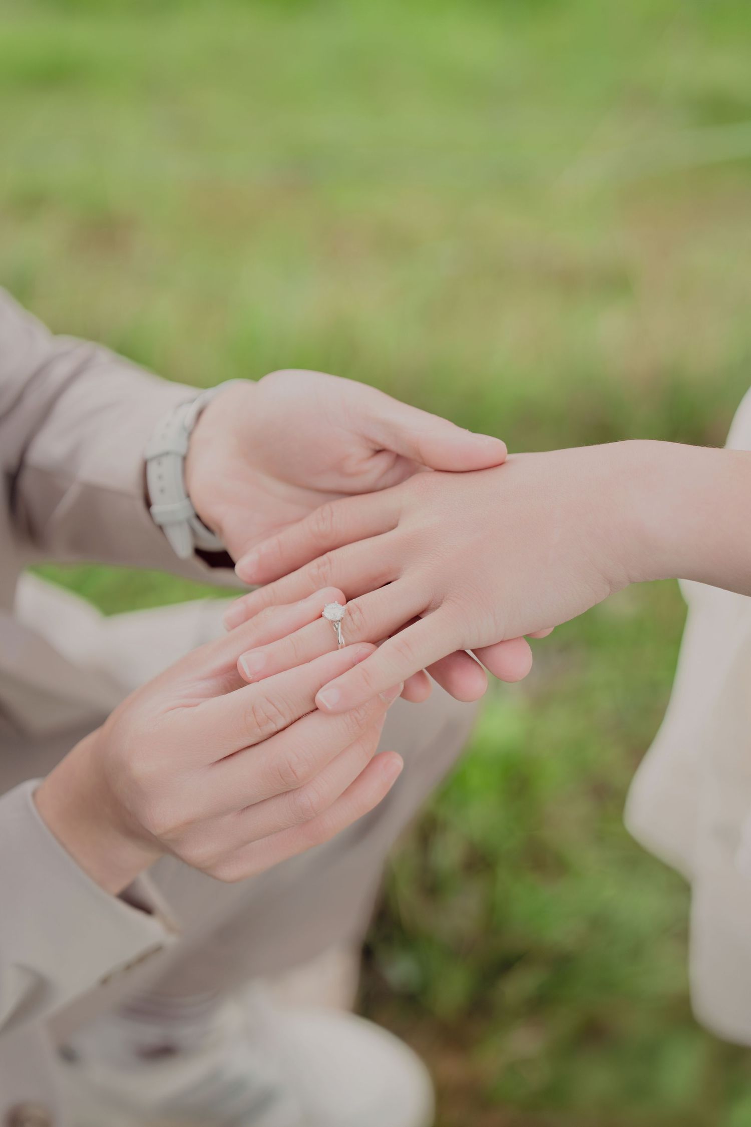 Close-up of a diamond engagement ring being placed on a bride's finger against a green grass background.
