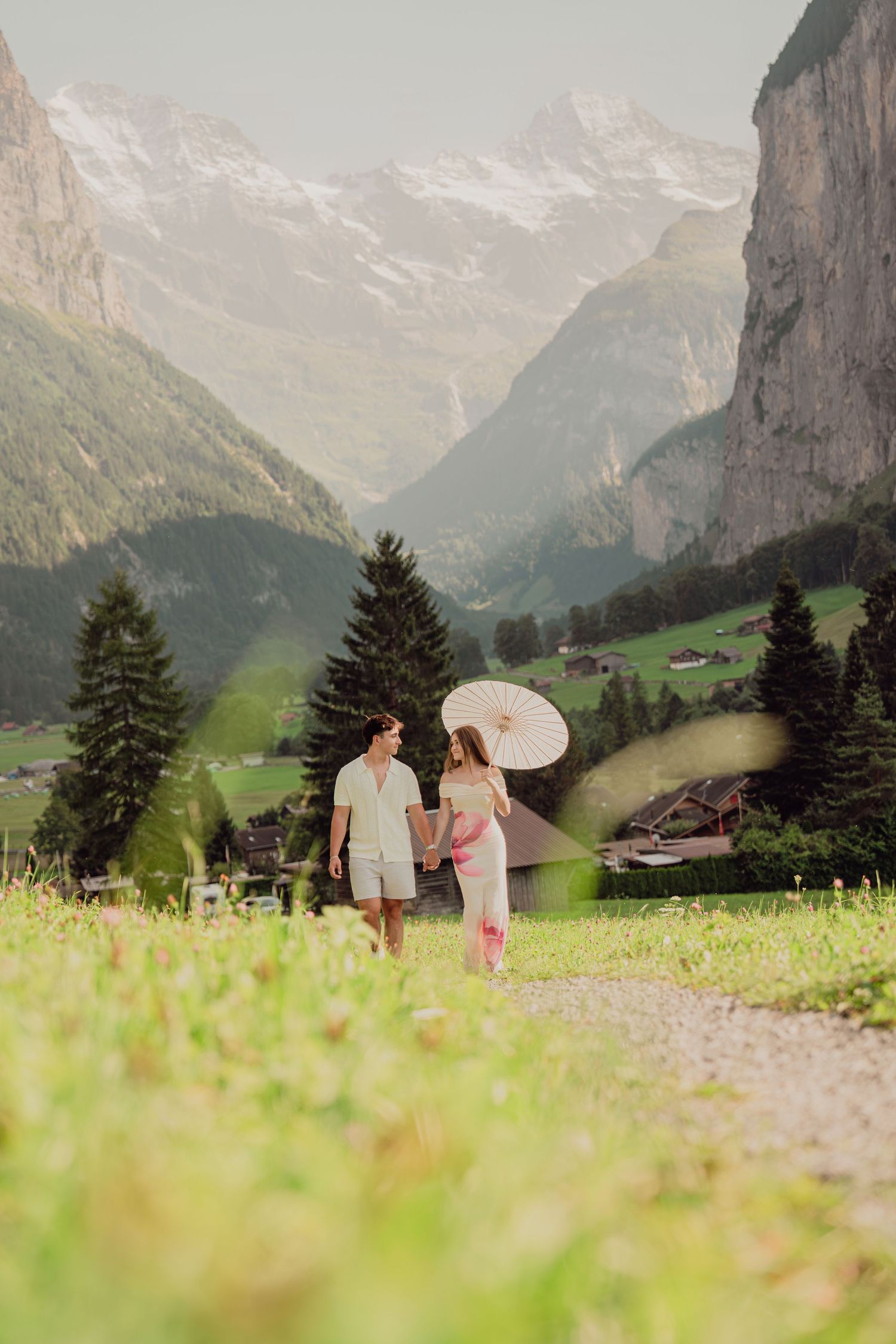 Couple holding hands and walking through a green alpine meadow with Lauterbrunnen Valley behind them.