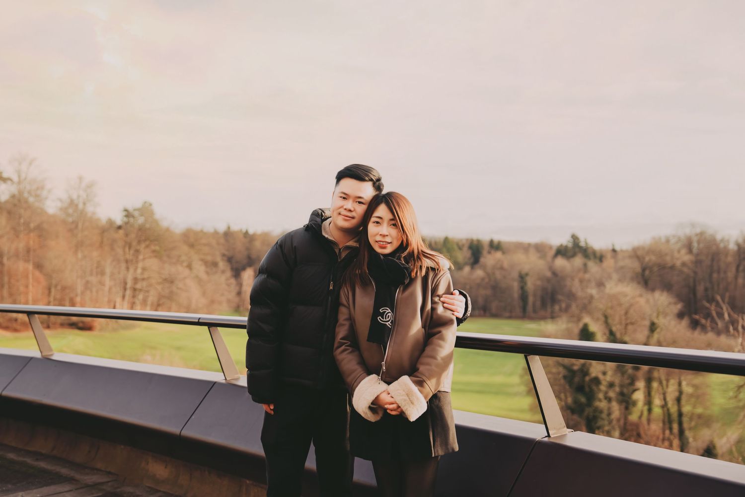 Asian couple cuddling together on an outdoor terrace with autumn forest landscape in background.