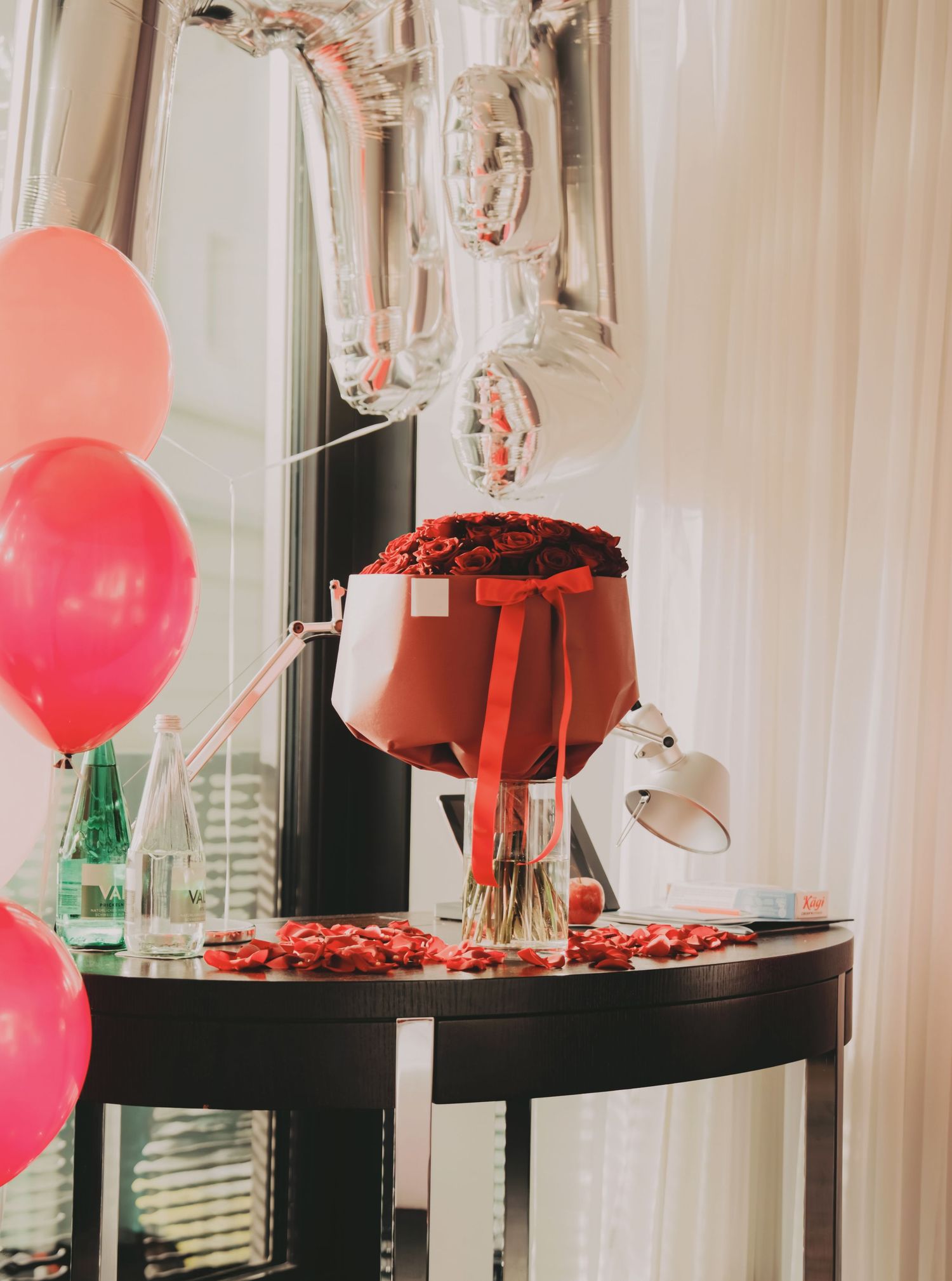 Elegant red rose bouquet arrangement with pink and silver balloons on table.