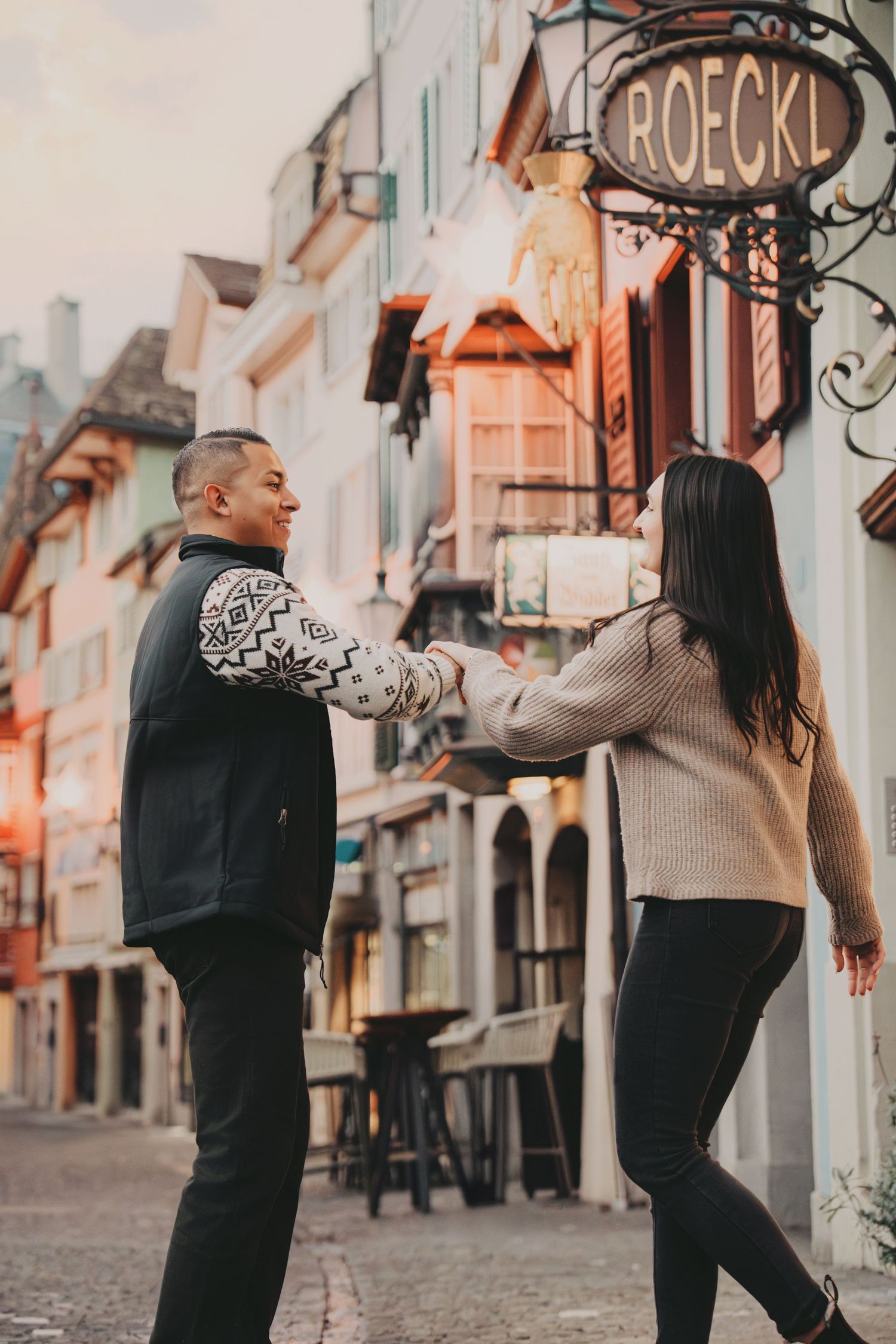 Playful couple holding hands while walking along a charming European street in Zurich, Switzerland.