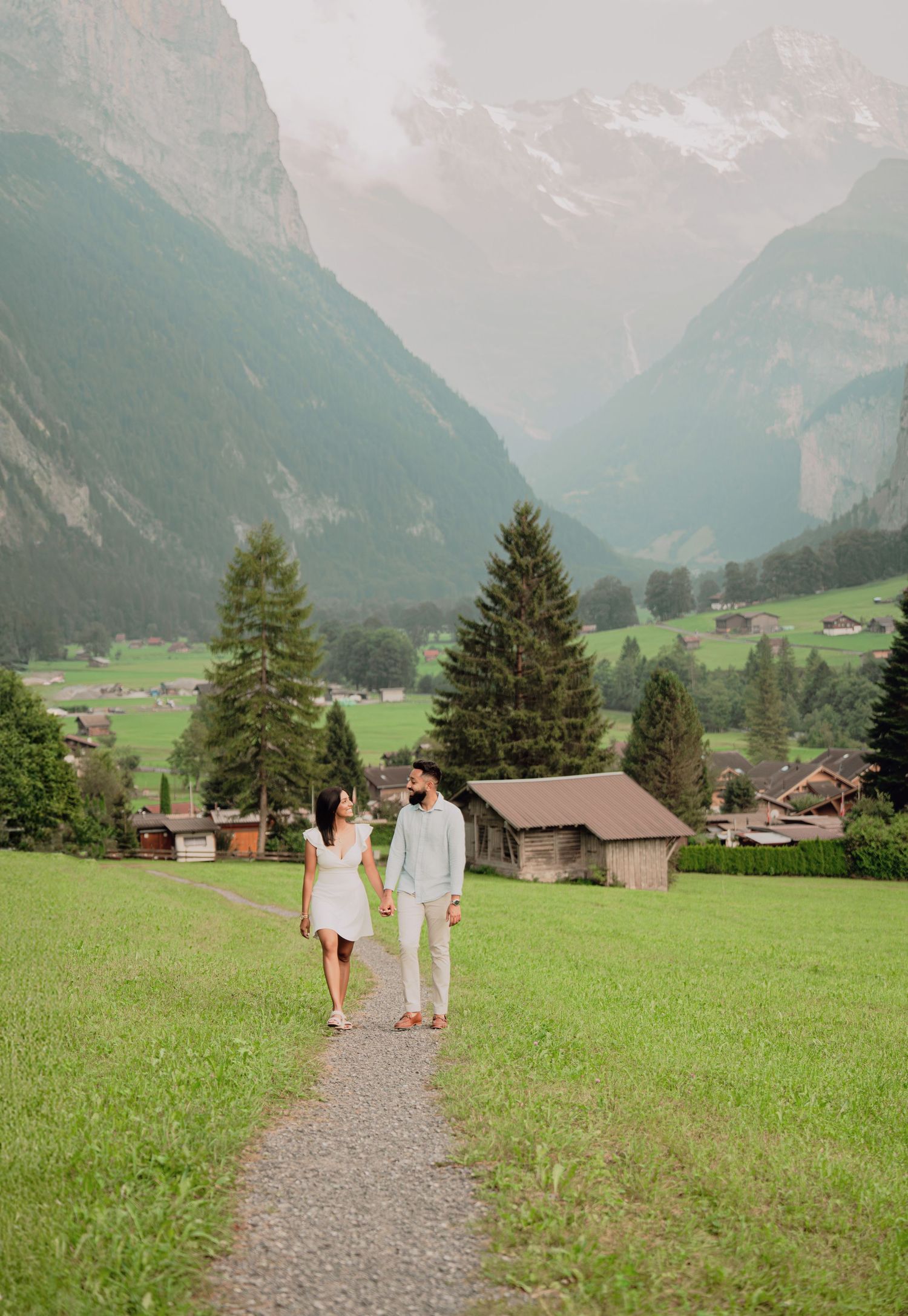 Young couple strolling along a scenic gravel path in a stunning Swiss Alpine valley with green meadows.