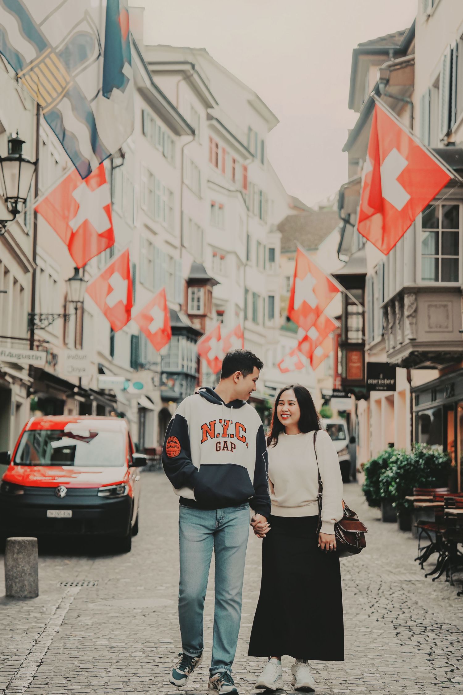 Smiling couple walking hand in hand down a Swiss old town street decorated with vibrant Swiss flags.