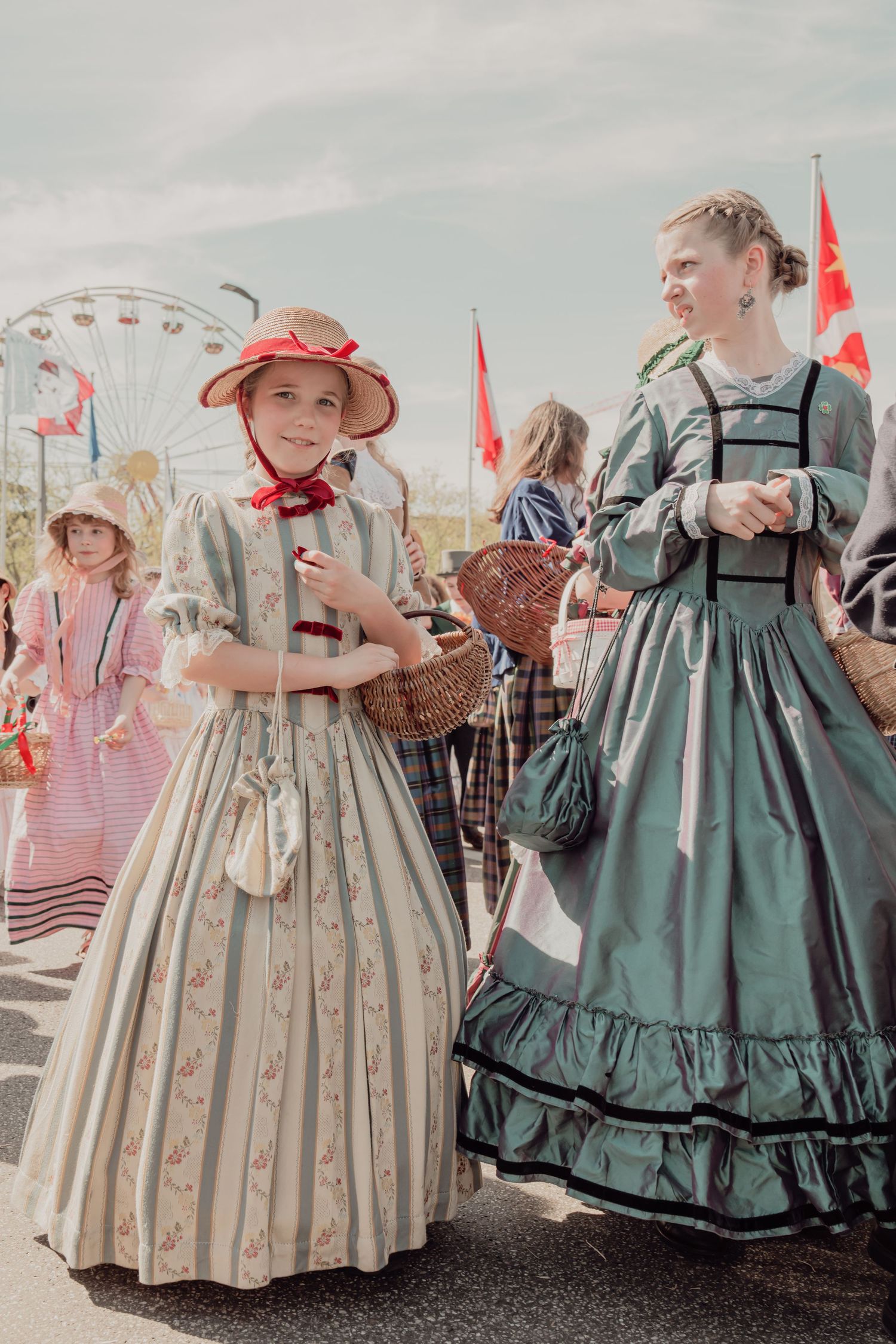 Two girls in vintage 19th century dresses and bonnets at historical costume parade.