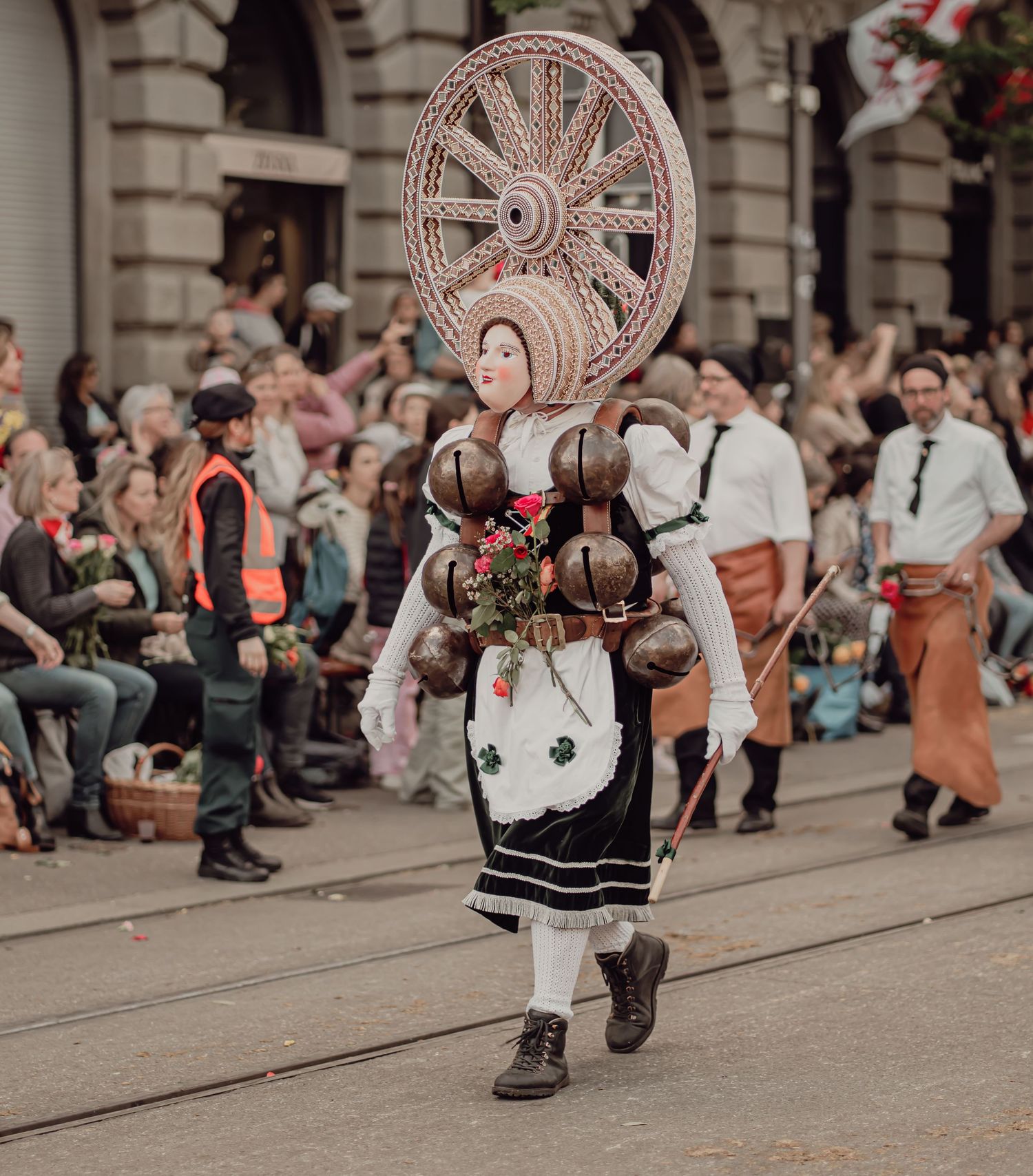 Woman in traditional Swiss folk costume wearing large spinning wheel headdress in parade.
