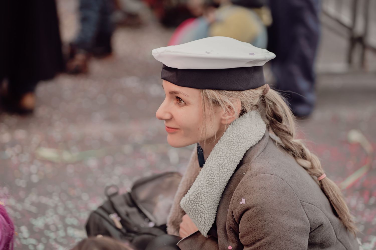 Blonde woman in military-style costume with sailor cap smiles at a carnival parade.