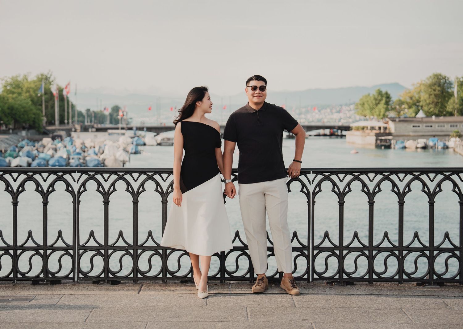 Smiling couple standing together by decorative iron fence with Zurich lake views behind them.