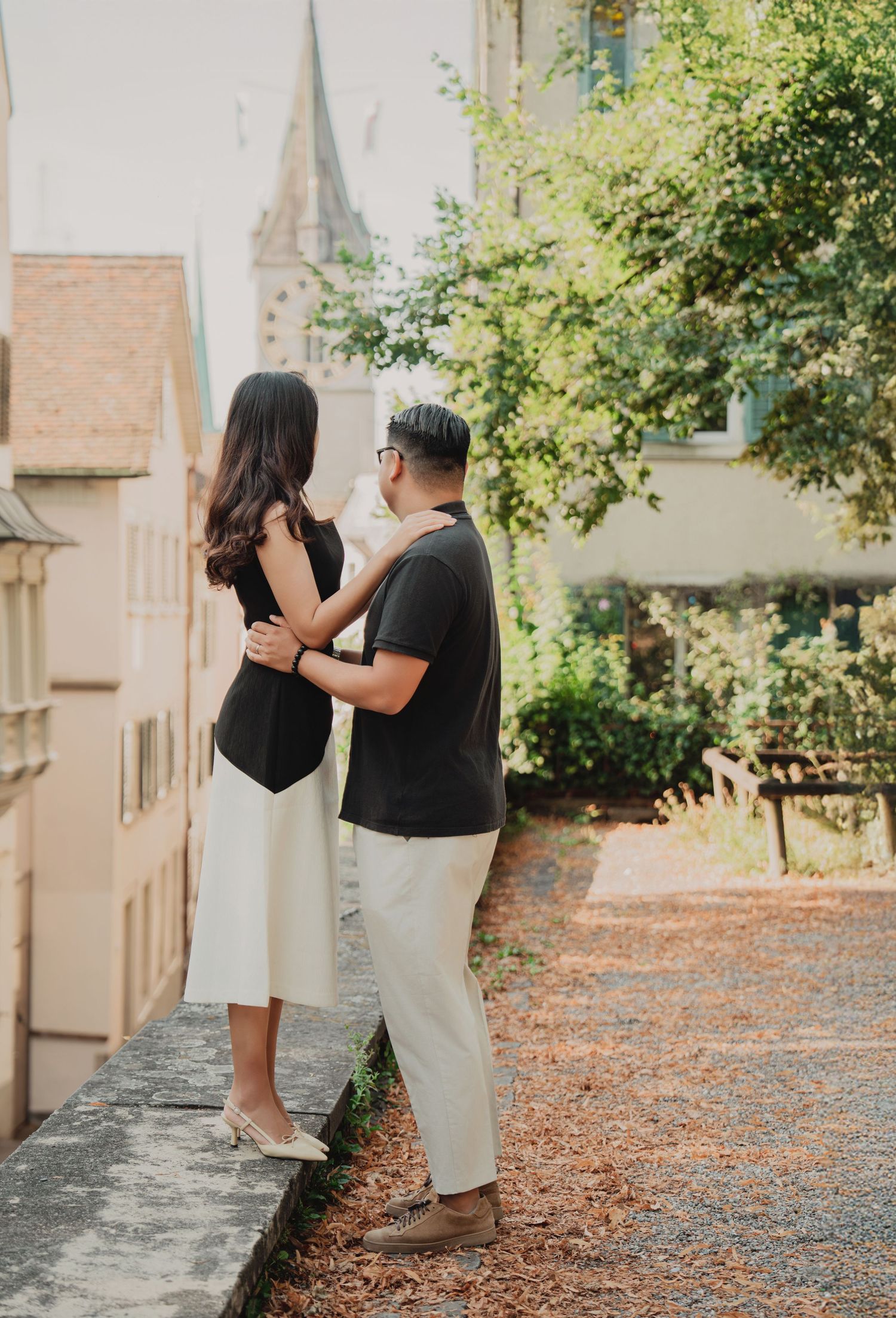 A couple shares a romantic embrace while overlooking a European cityscape with a church steeple.