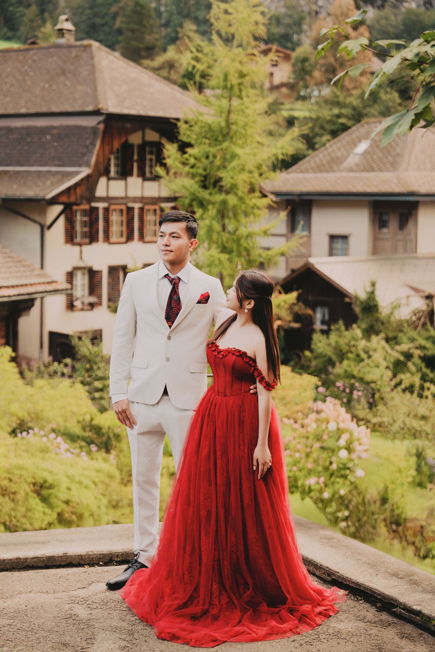 Couple posing in red gown and white suit before charming Swiss alpine village houses.