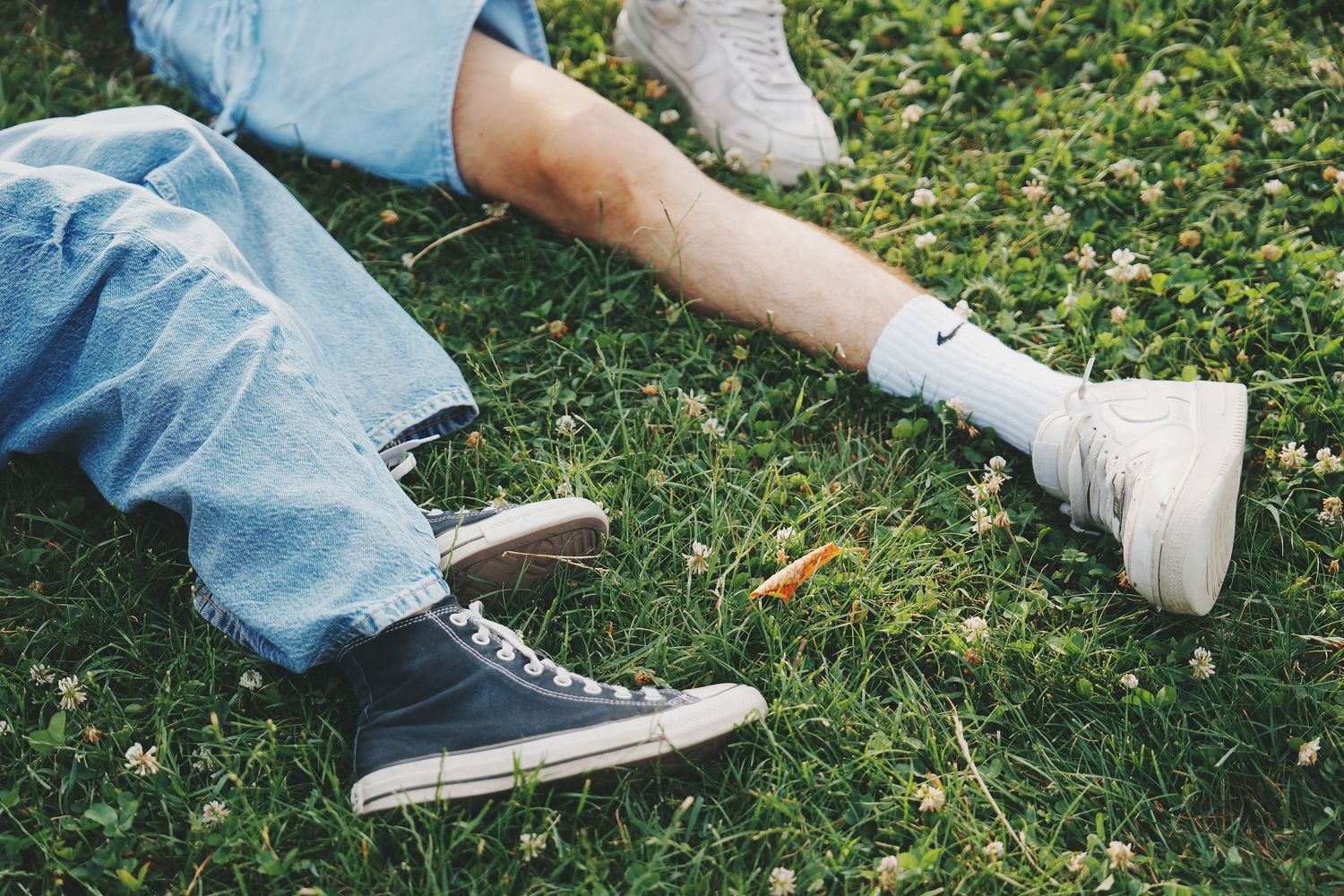 Close-up of couple's legs lying on green clover grass wearing jeans and white sneakers.