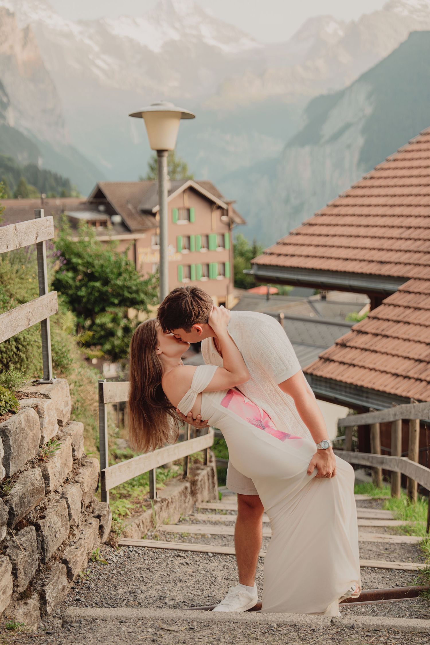 Man dipping woman in passionate kiss on stone steps in picturesque Swiss mountain village.