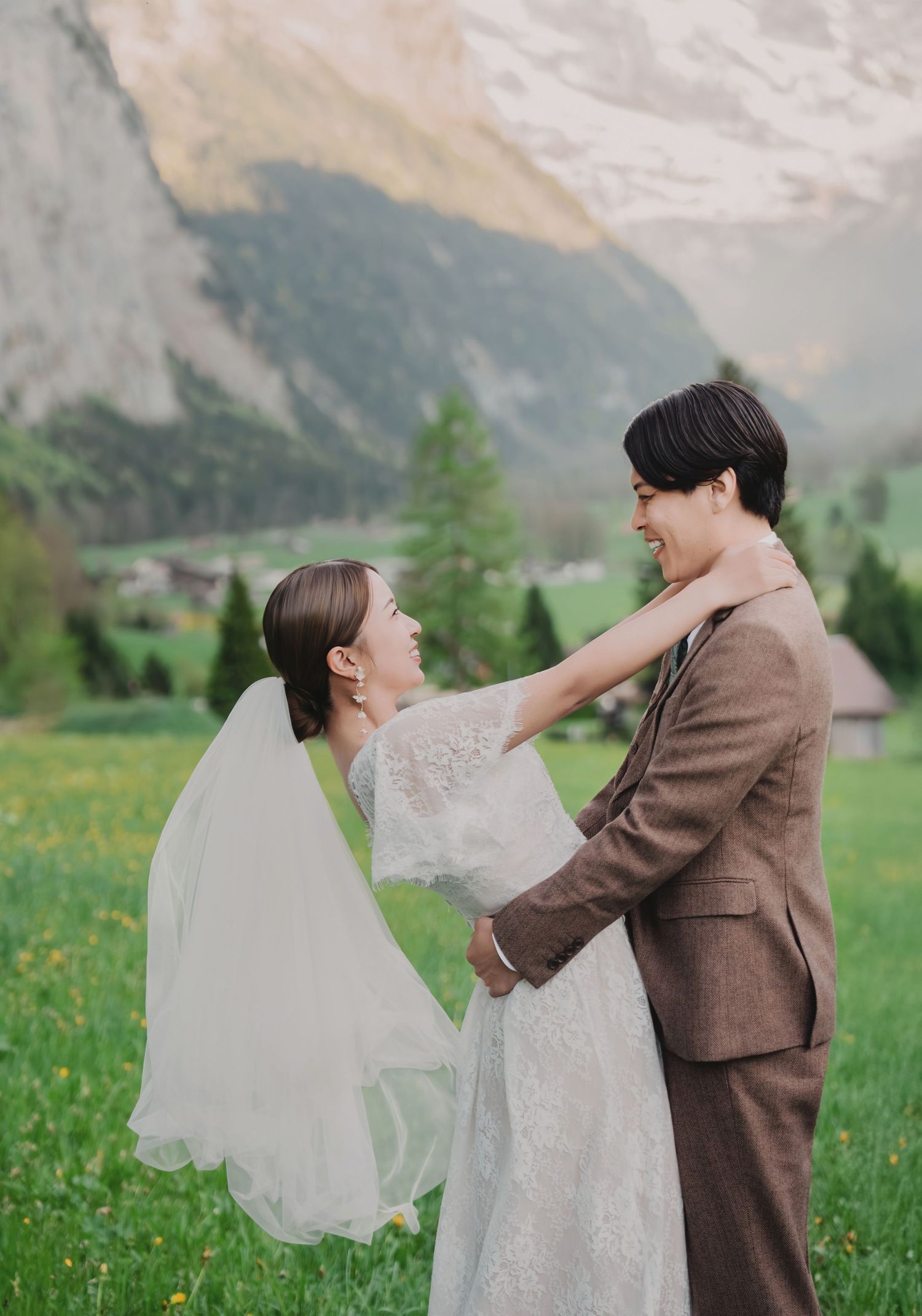 Bride and groom smiling and embracing in a vibrant green alpine meadow with stunning Swiss mountain scenery.