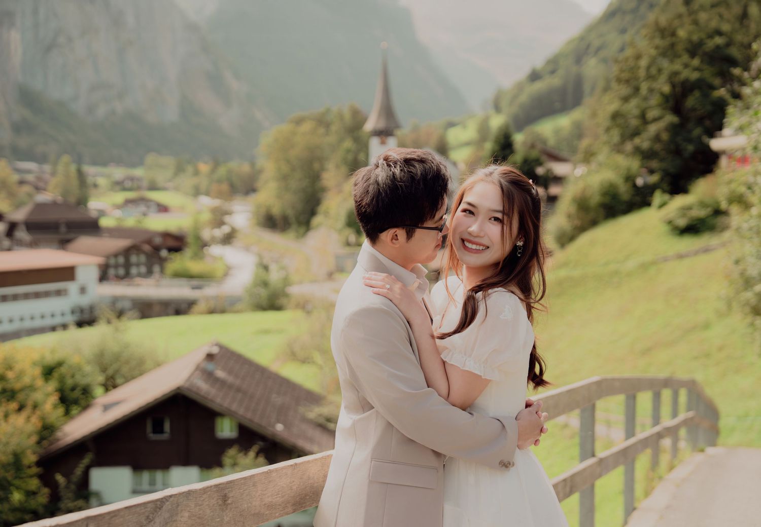 Joyful bride and groom sharing a romantic hug with Swiss alpine village scenery in the background.