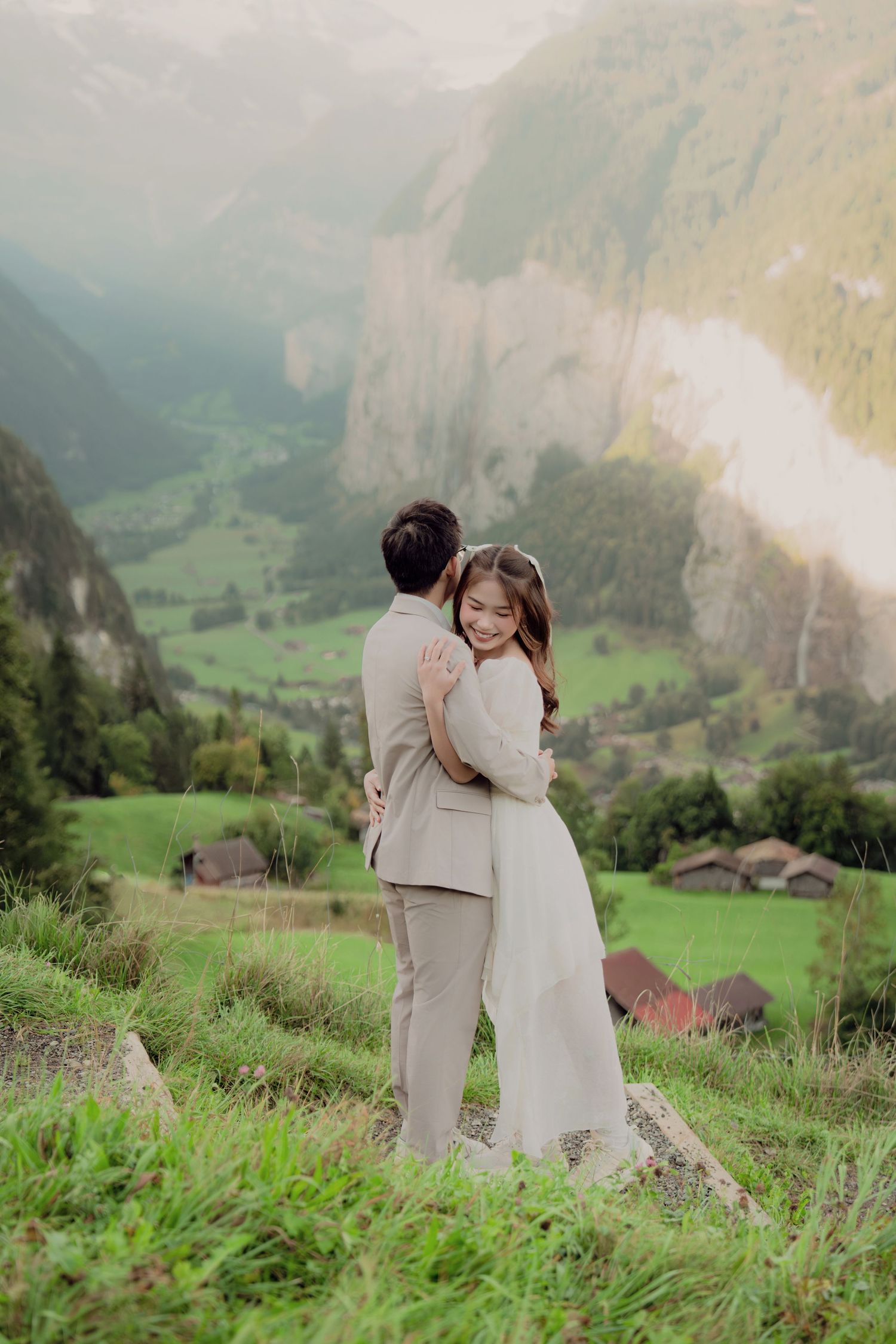 Happy couple sharing romantic embrace on rocky overlook above scenic Swiss alpine valley.