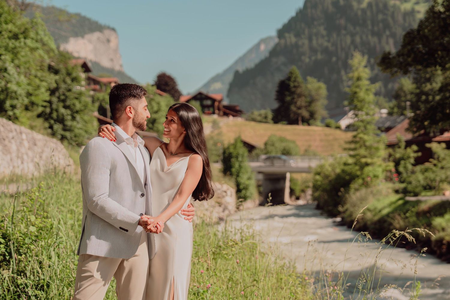 Romantic couple in neutral tones standing together by a river in an alpine village.