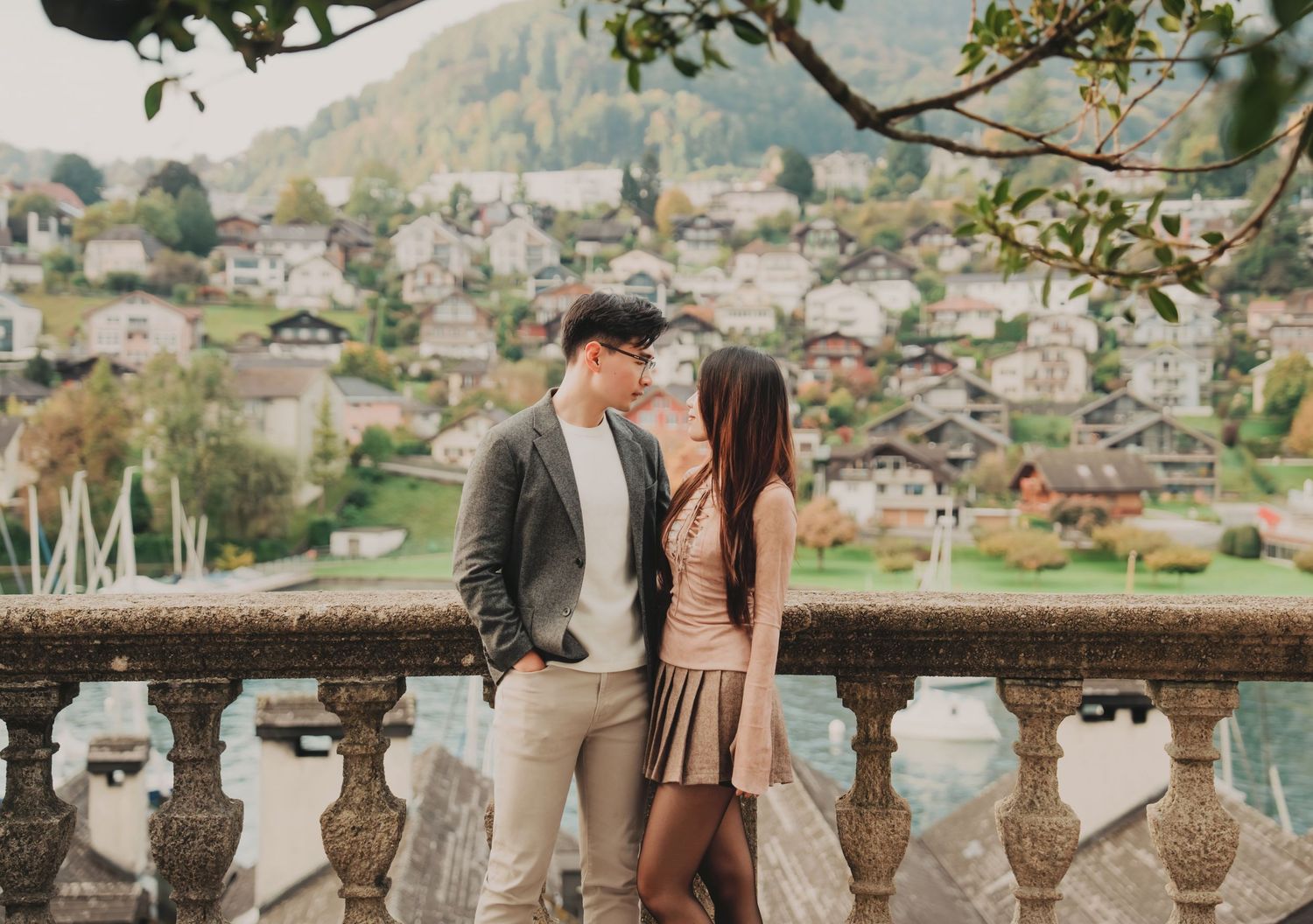 Young couple gazing at each other on elegant balcony with charming Alpine lakeside town behind.