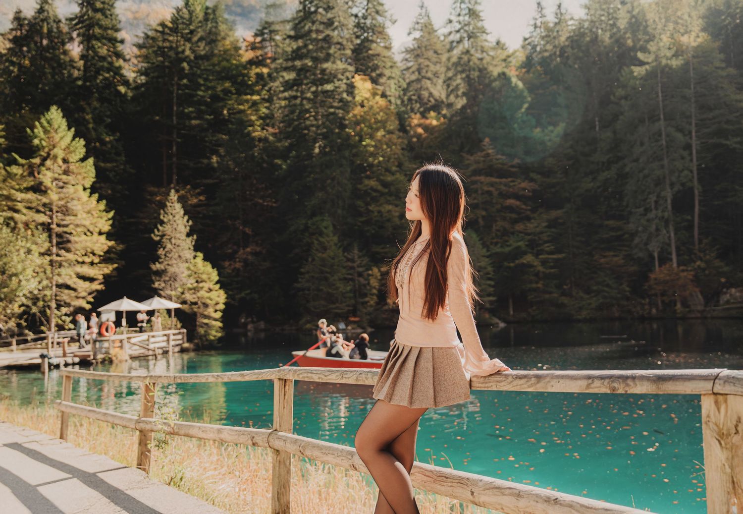 Young woman in mini skirt standing by wooden railing overlooking turquoise mountain lake.