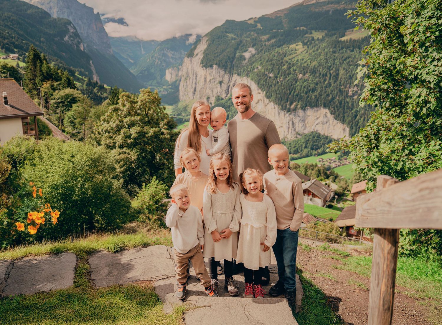 Family of eight with parents and six young children smiling before a stunning Swiss waterfall valley.