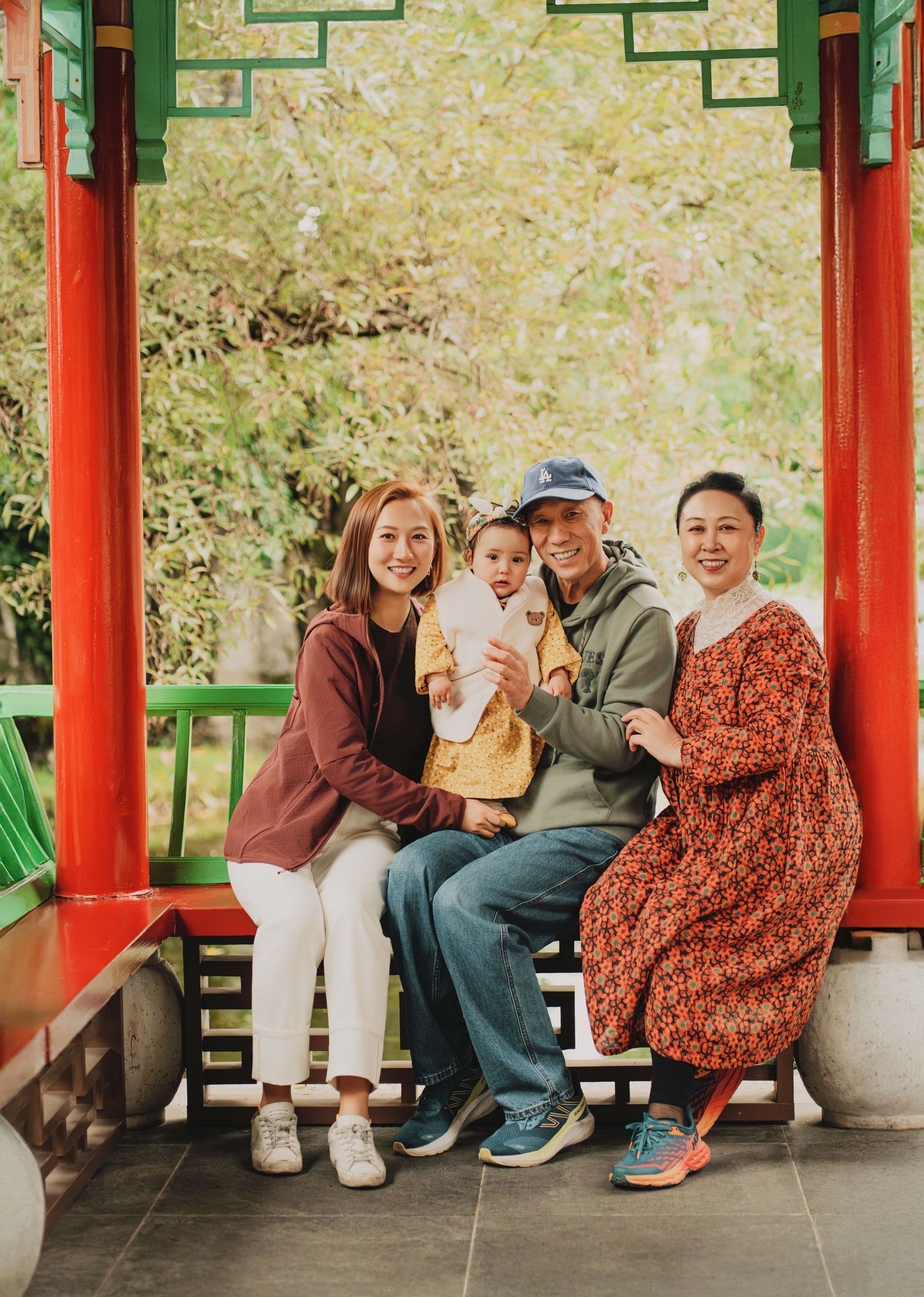 Four family members posing with a baby in a red Chinese garden pavilion.