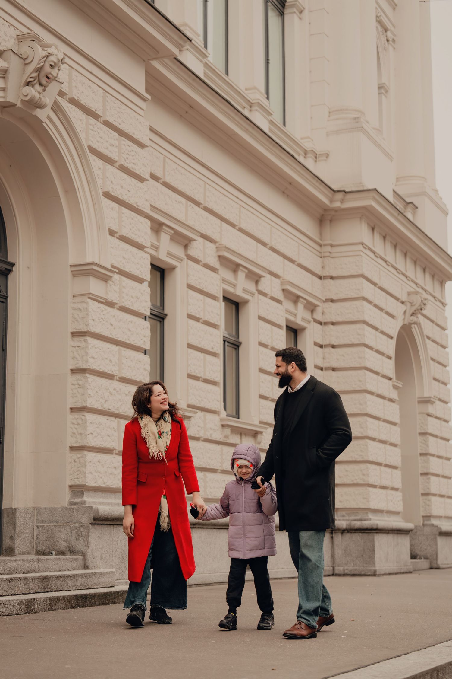 Family holding hands and walking together along a neoclassical building exterior.