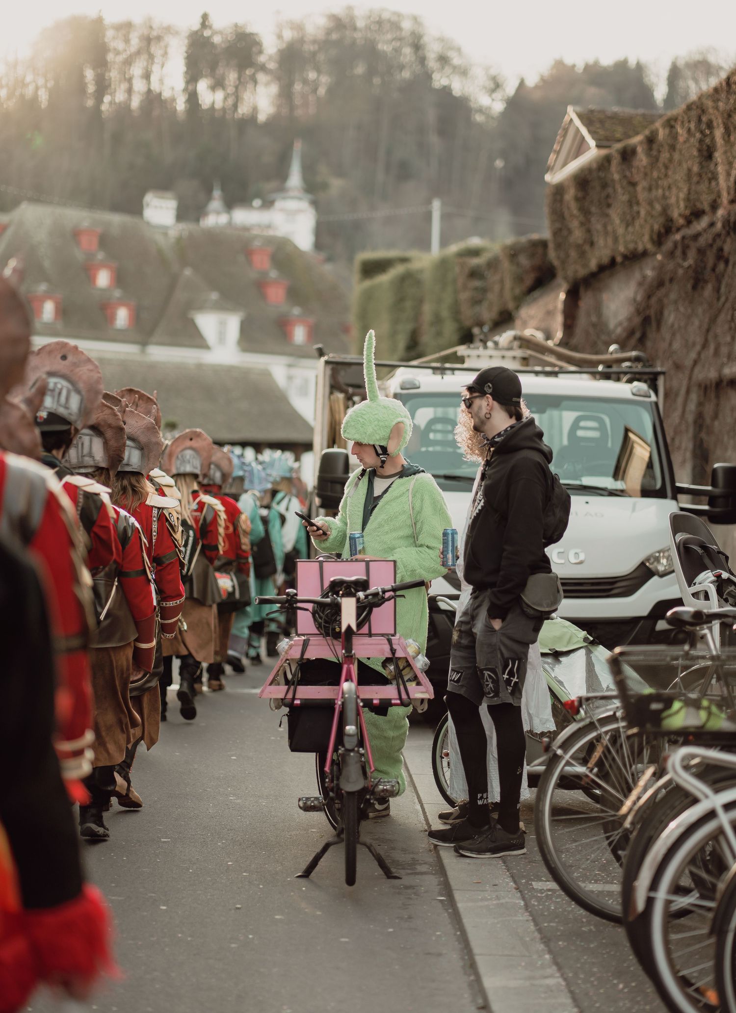 Colorful carnival participants in costumes gather on a street near historic buildings.
