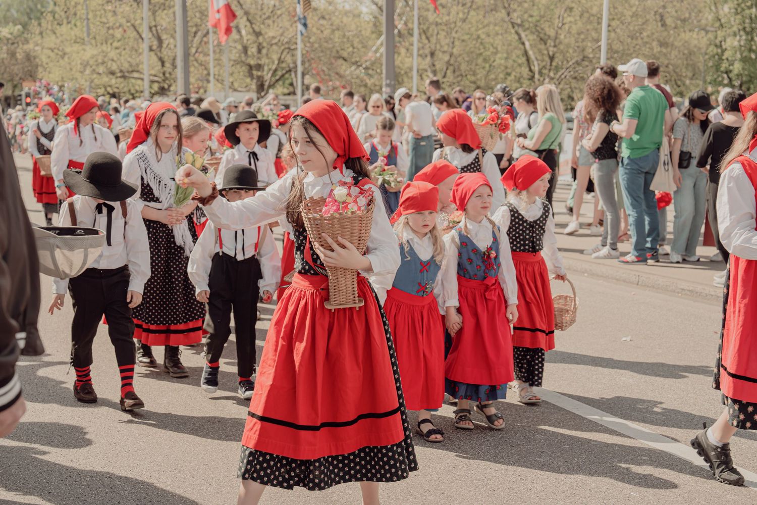 Children and adults in red and white traditional Swiss folk costumes dancing and performing at an outdoor festival.