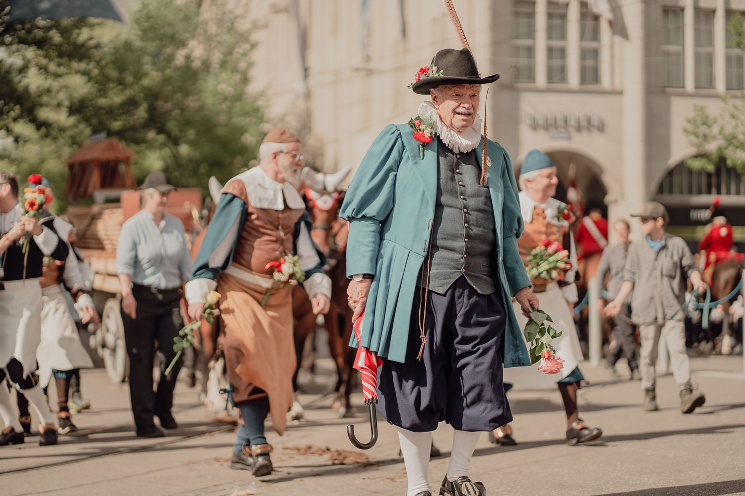 A bearded man in historic blue costume smiles while walking in a traditional street parade.