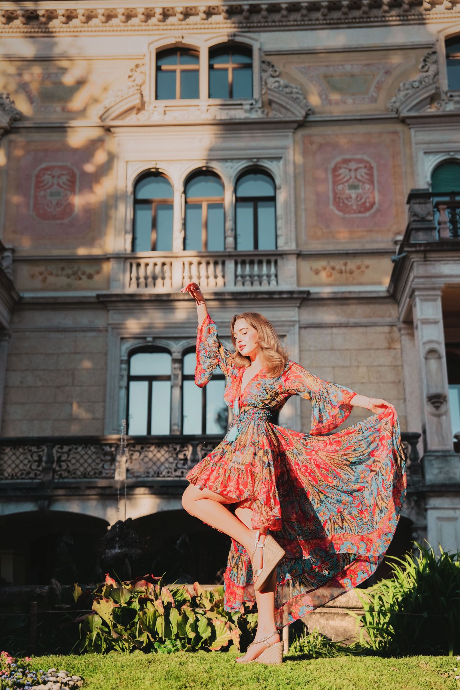 Woman in colorful floral dress twirling in front of ornate building.